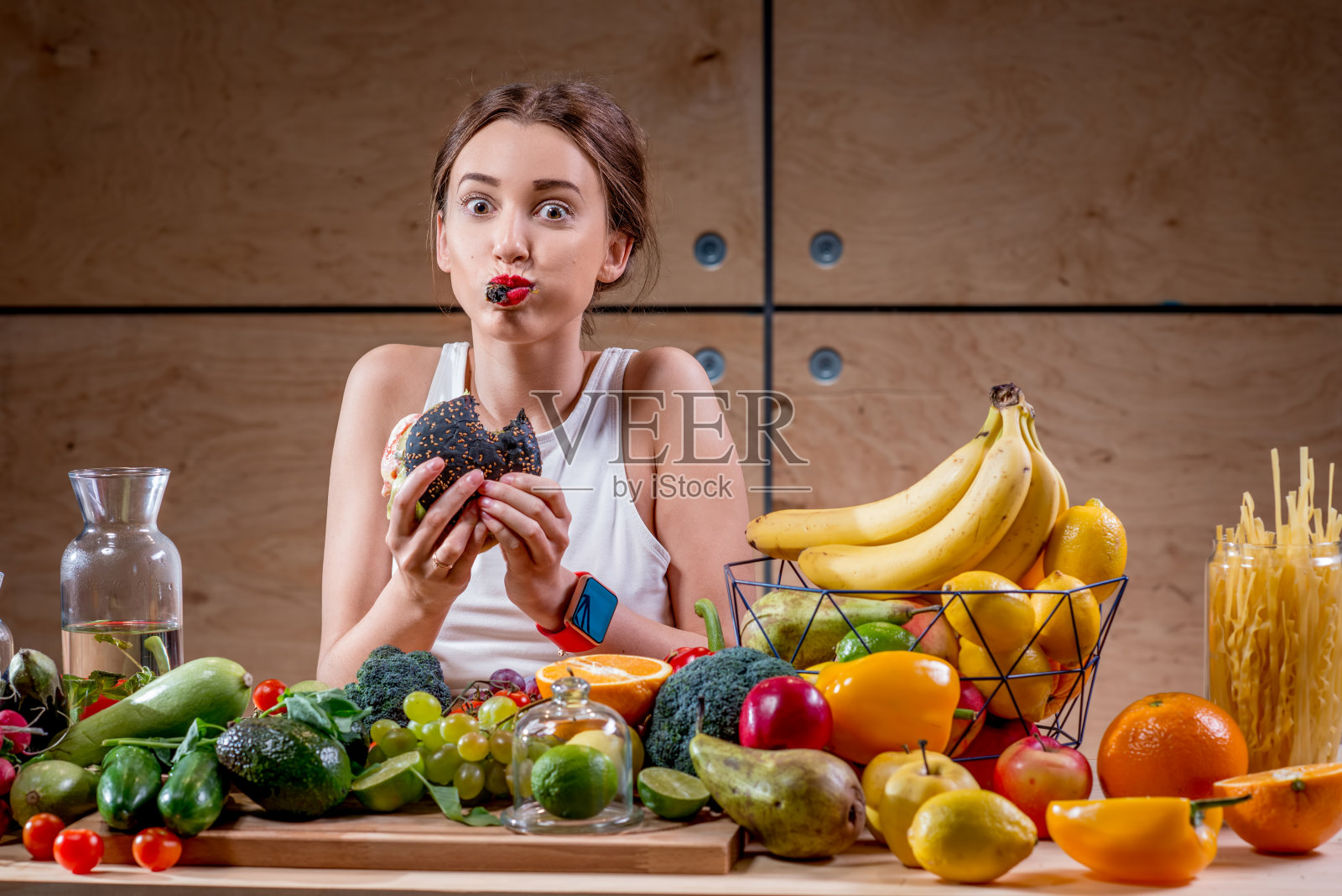 坐在摆满健康食品的桌子前吃汉堡的女人照片摄影图片