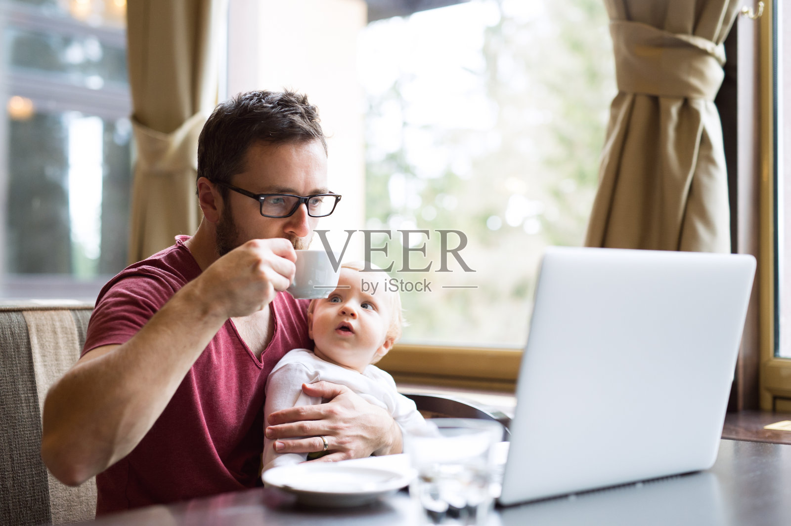 一个男人拿着笔记本在咖啡馆喝咖啡，抱着他的儿子照片摄影图片