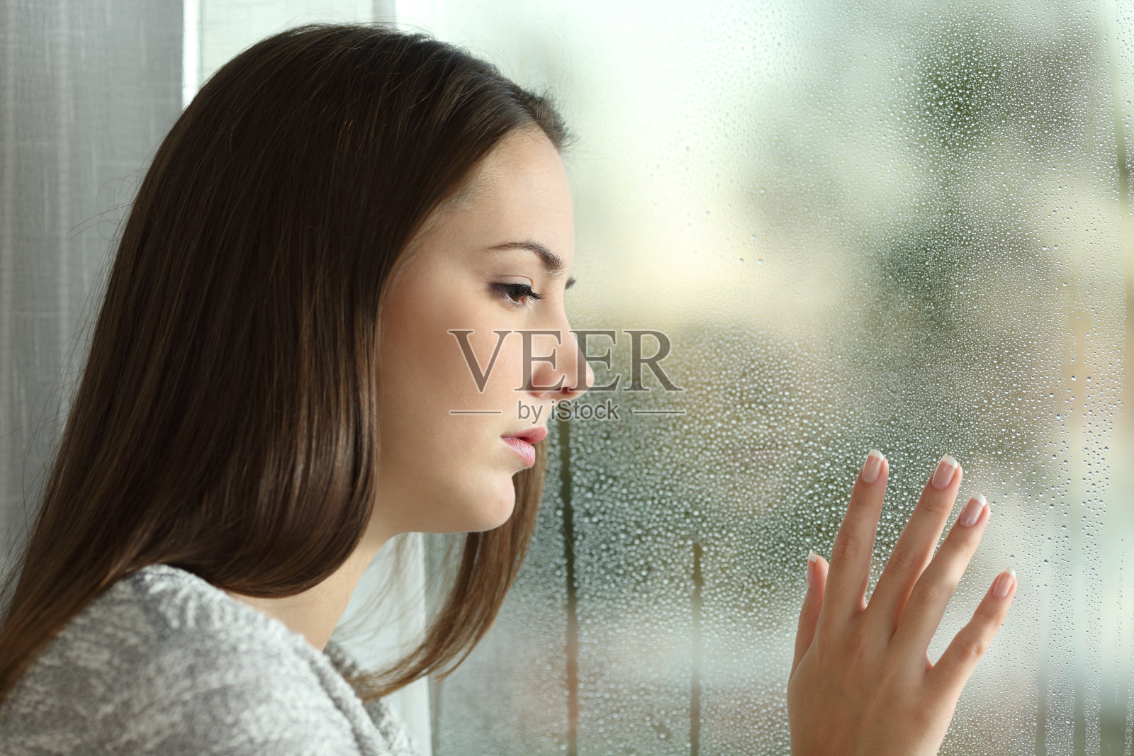 悲伤的女人透过窗户看雨照片摄影图片