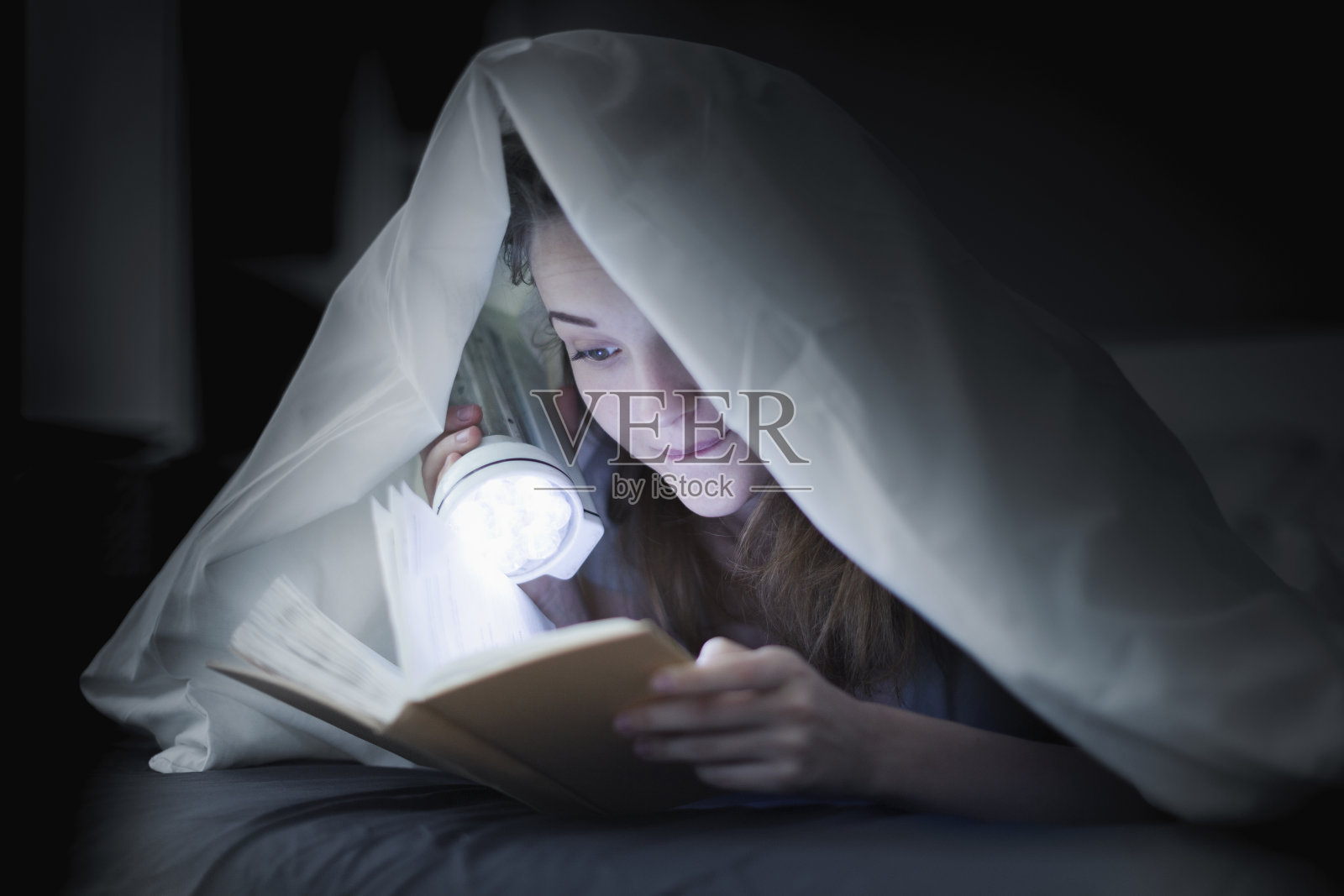 一个十几岁的女孩在床上盖着被子看书照片摄影图片
