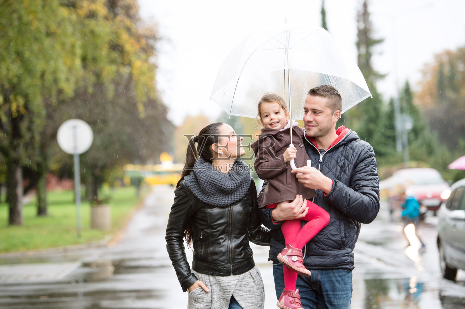 家人带着女儿撑着雨伞在雨天散步。照片摄影图片