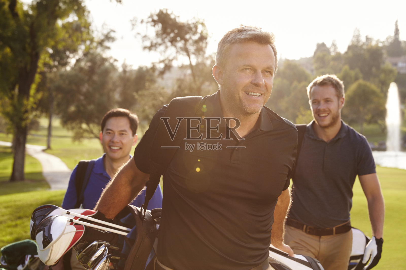一群男性高尔夫球手背着包沿着球道行走照片摄影图片