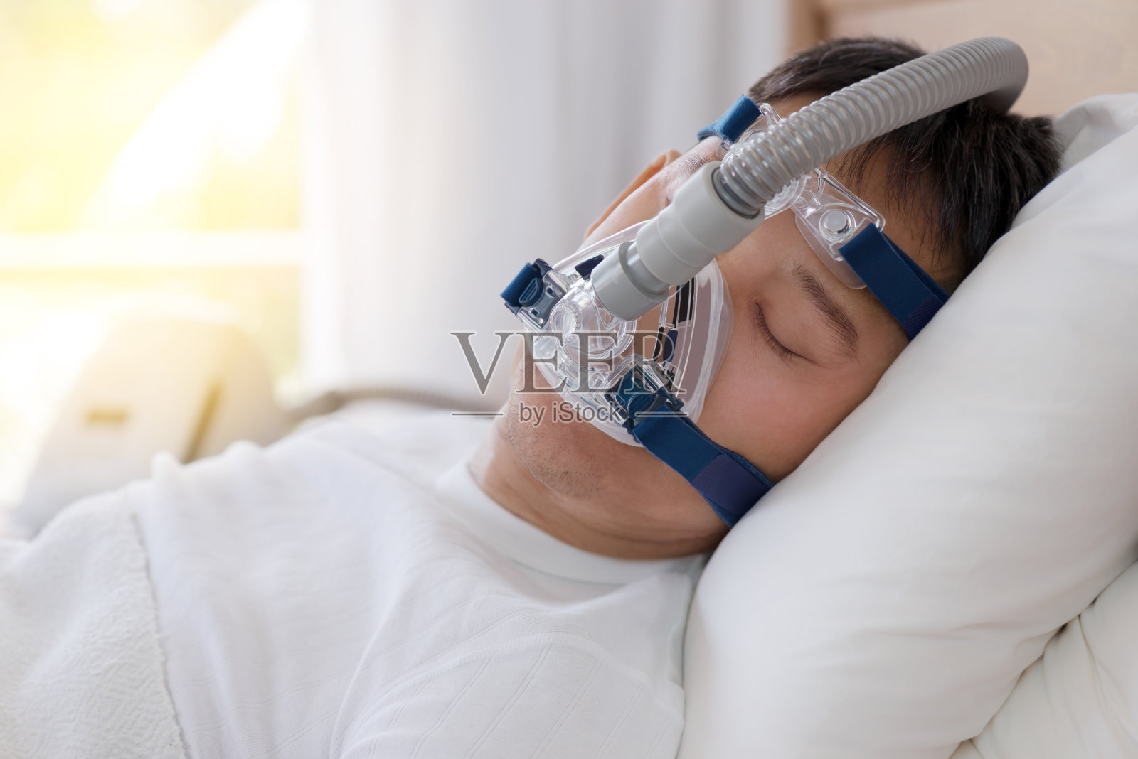 睡眠呼吸暂停治疗，男人戴着呼吸面罩睡在床上。照片摄影图片