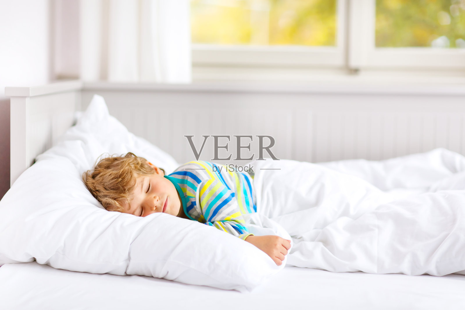 无忧无虑的小男孩睡在床上五颜六色的睡衣。照片摄影图片