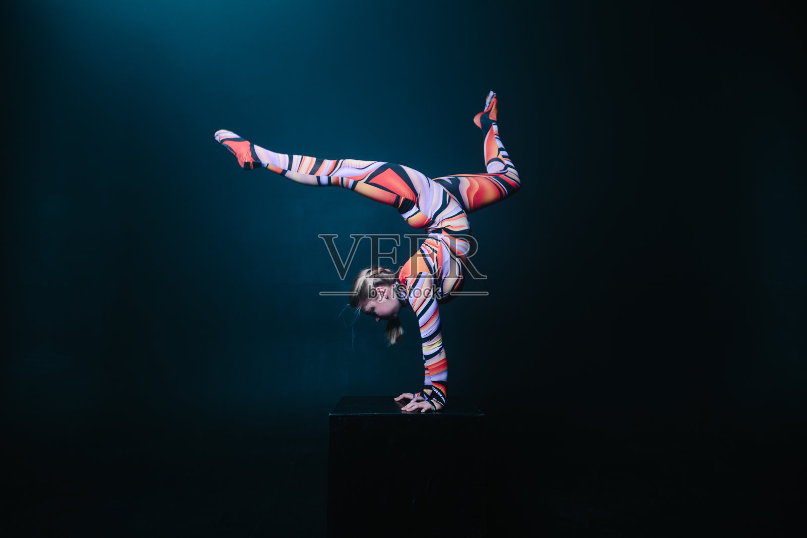 灵活的马戏团杂技演员在一个立方体上做平衡倒立。照片摄影图片