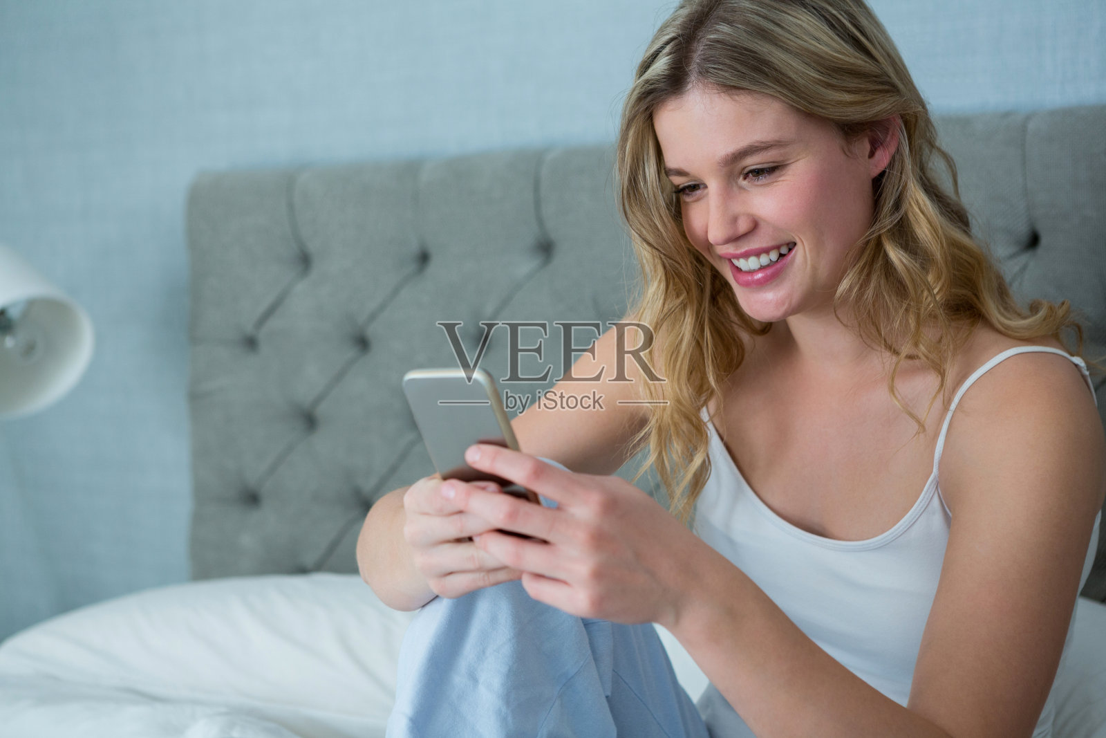 微笑的女人在床上用手机照片摄影图片