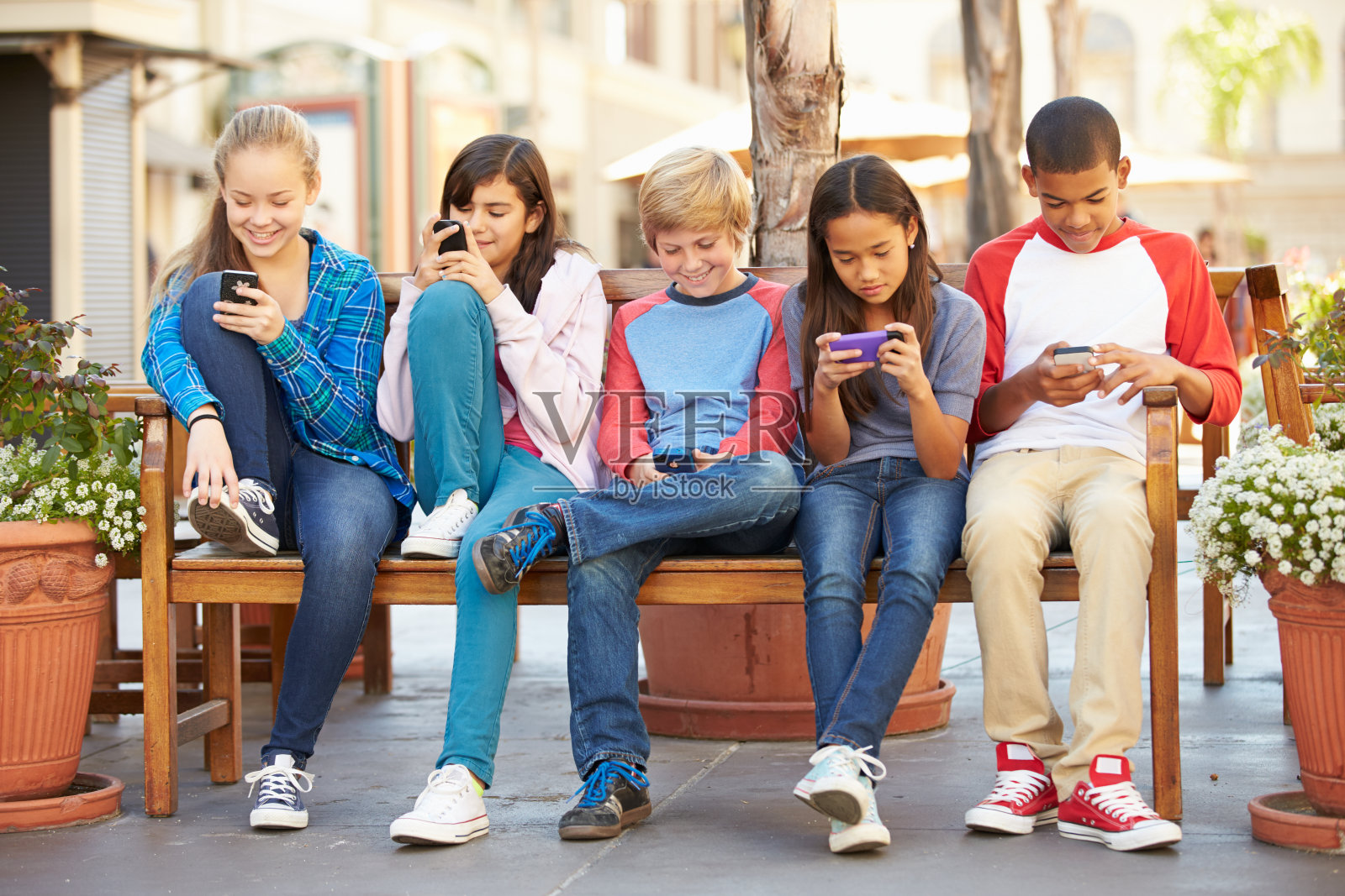 一群坐在商场里用手机的孩子照片摄影图片