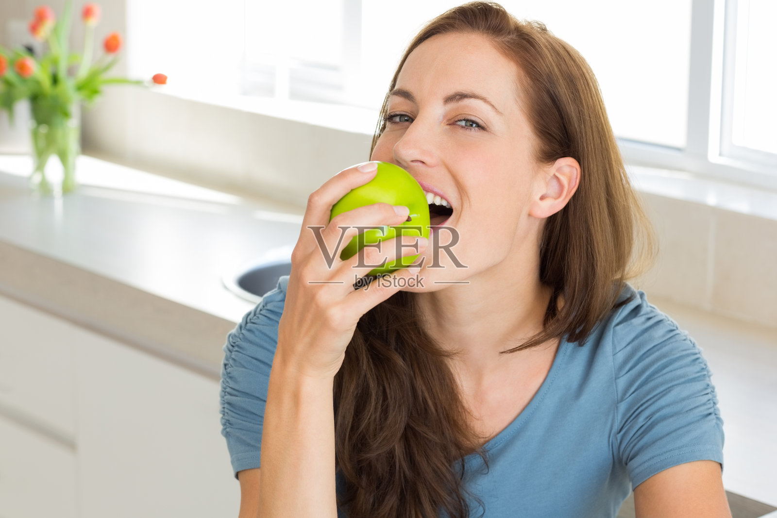 微笑的年轻女子在厨房吃苹果照片摄影图片