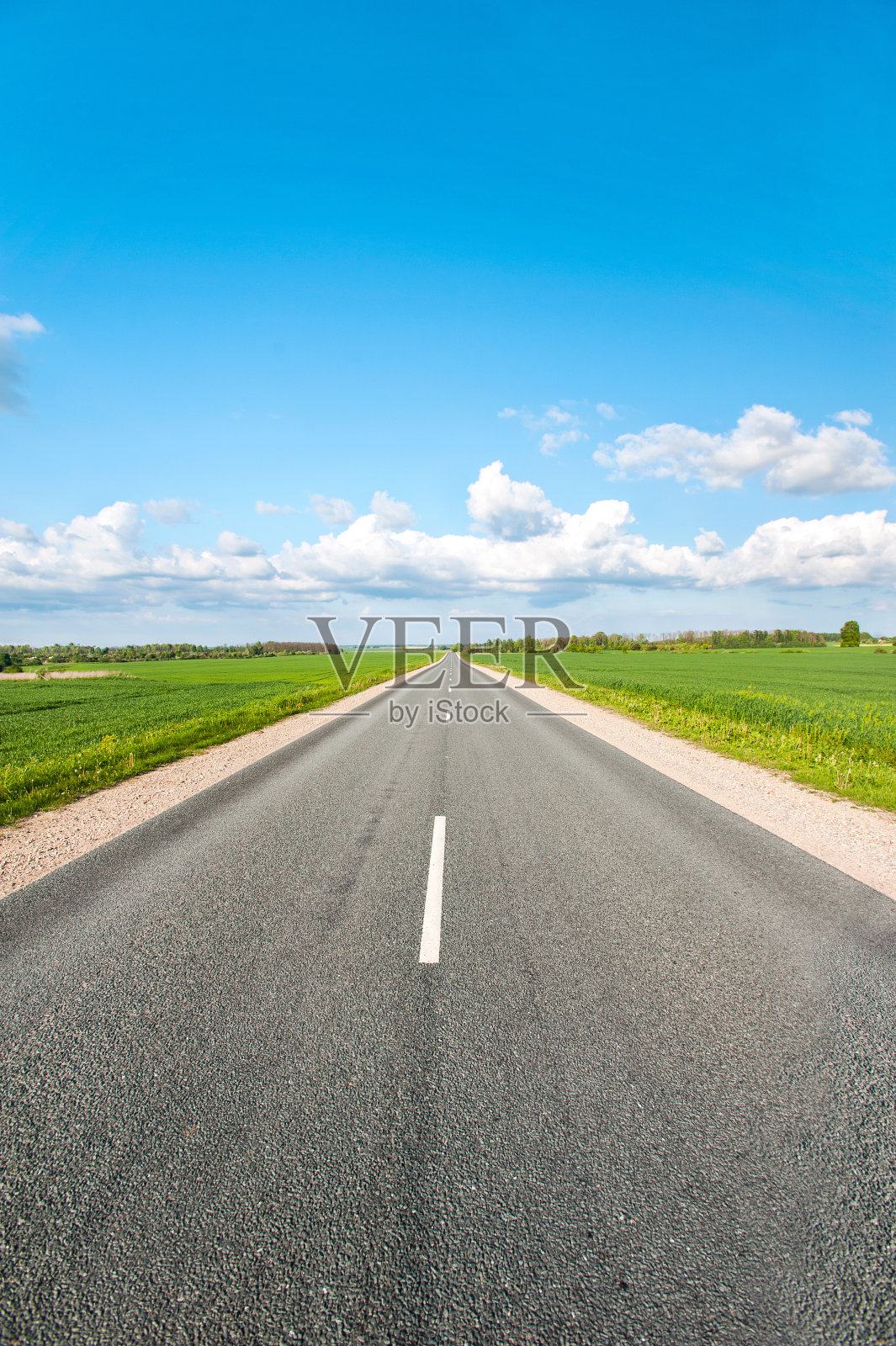 柏油路在绿色的田野上，在蓝色多云的天空背景下照片摄影图片