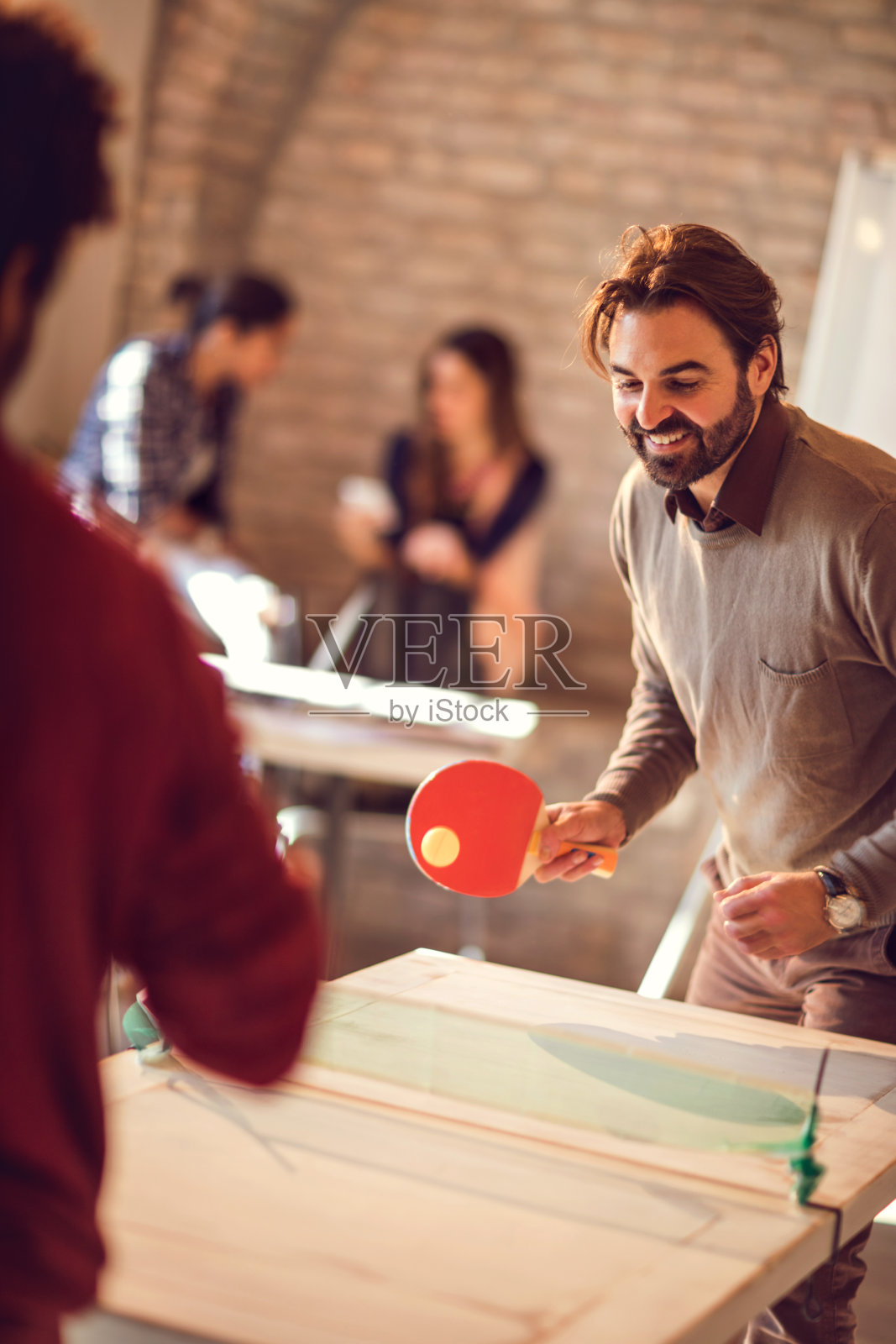 快乐的商人和他的同事在办公室打乒乓球。照片摄影图片