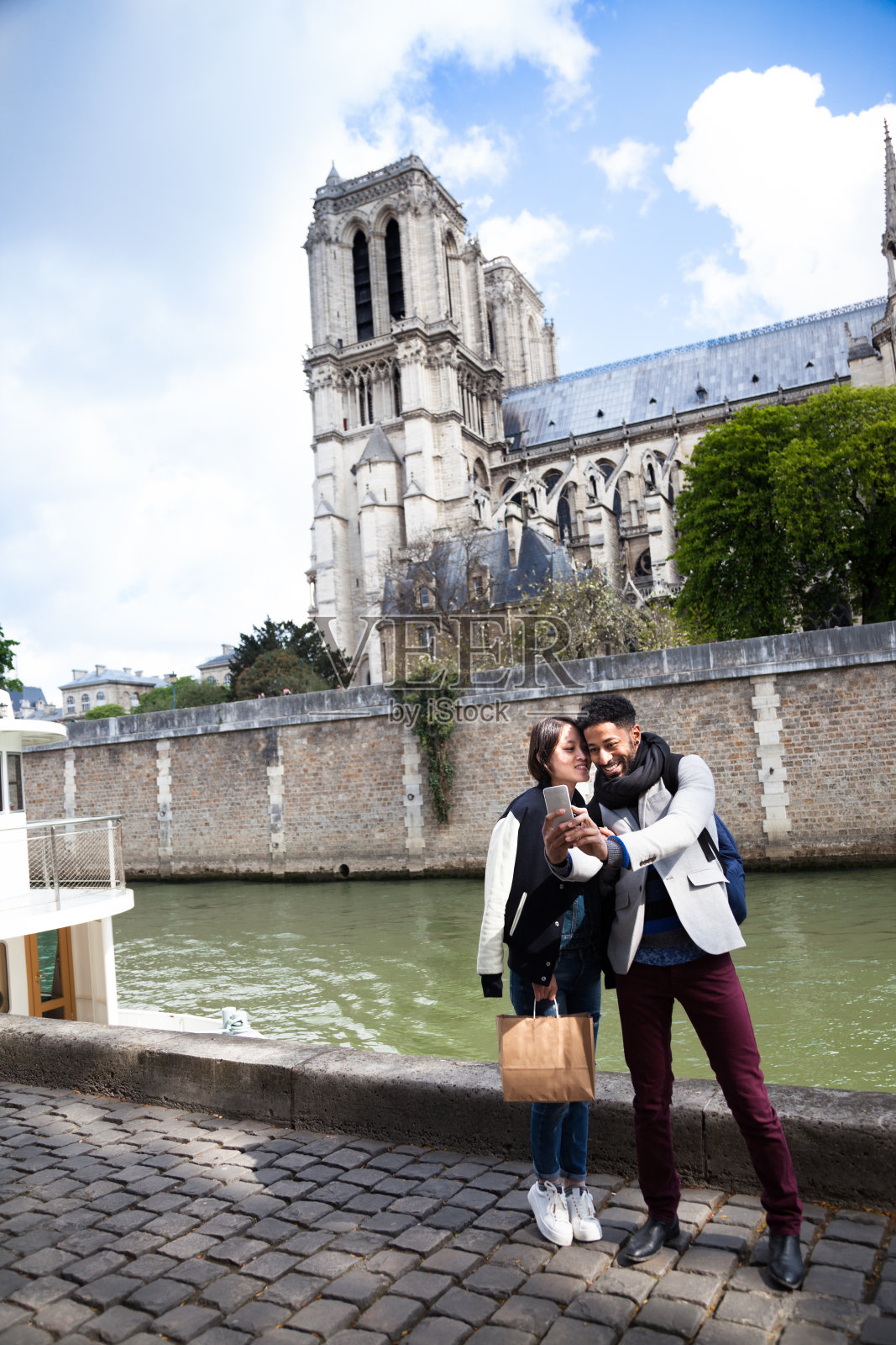 一对来自不同种族的年轻情侣在巴黎塞纳河边的圣母院合影照片摄影图片