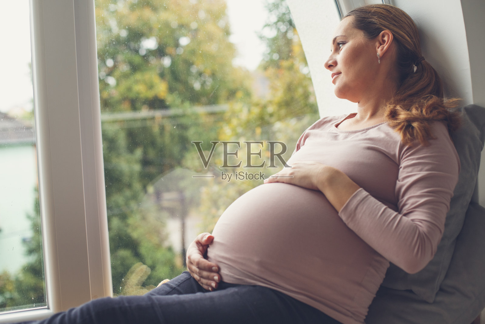 一个孕妇抱着肚子，从窗户往外看照片摄影图片
