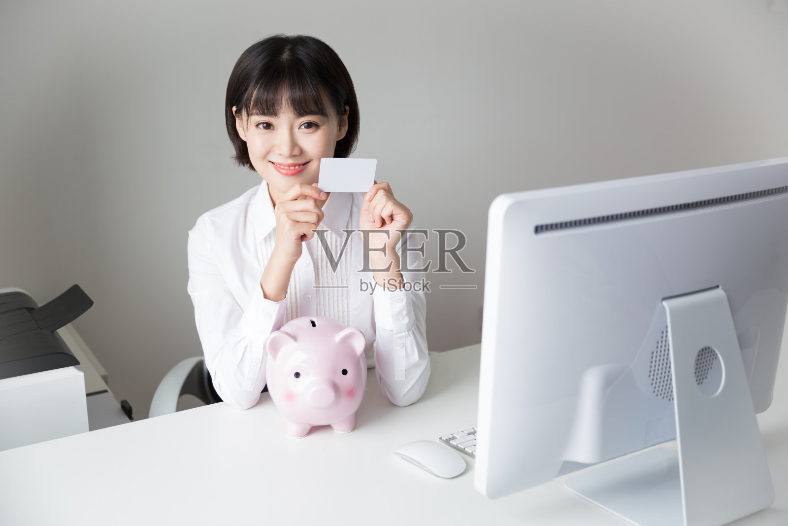 小女孩坐在办公室里，手里拿着小猪模型存钱罐照片摄影图片