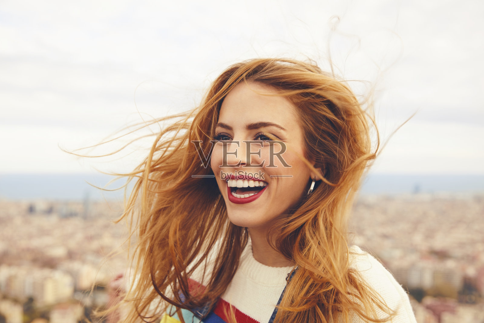 在城市风景的映衬下，一头乱发的快乐女人照片摄影图片