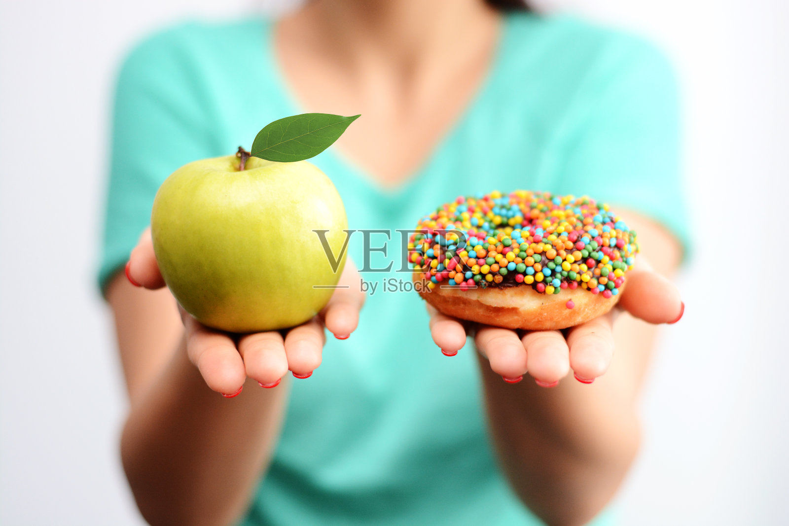 很难选择健康的食物概念，因为女人手里拿着一个绿苹果和一个热量炸弹甜甜圈照片摄影图片