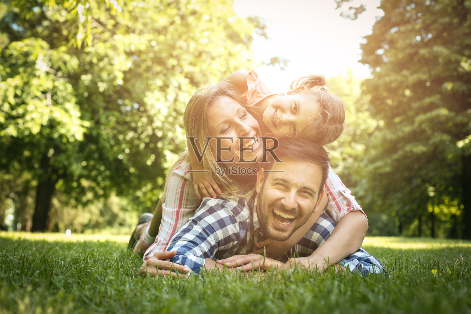 快乐的家庭一起享受在夏天的日子。一家人躺在草地上。母亲和女儿躺在父亲的背上。照片摄影图片