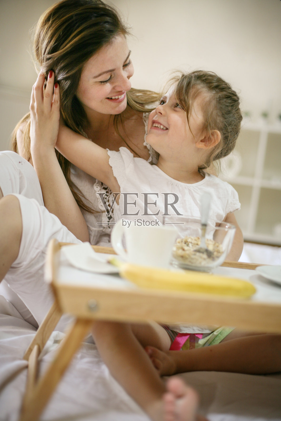 妈妈和她的小女儿在床上吃早餐。照片摄影图片