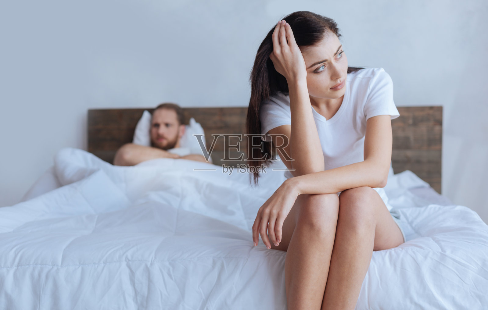 心烦意乱的女人坐在床上，身后是愤怒的丈夫照片摄影图片