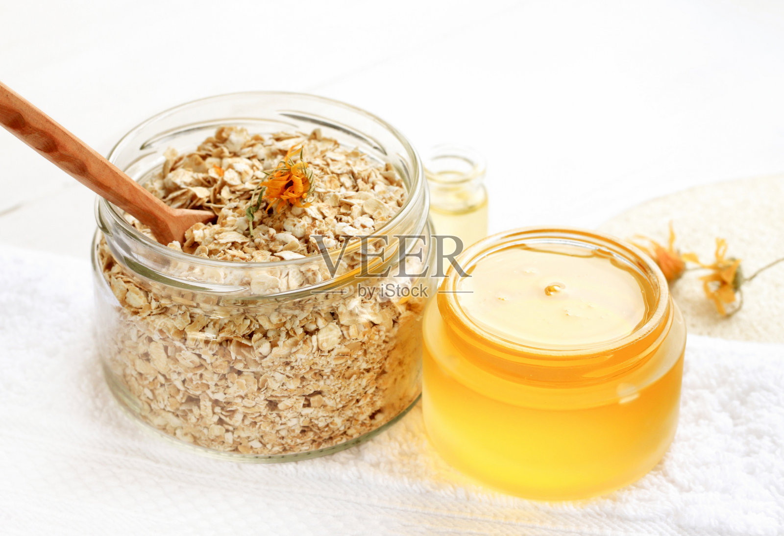 燕麦片和黄色蜂蜜的玻璃罐，白色的浴巾。照片摄影图片