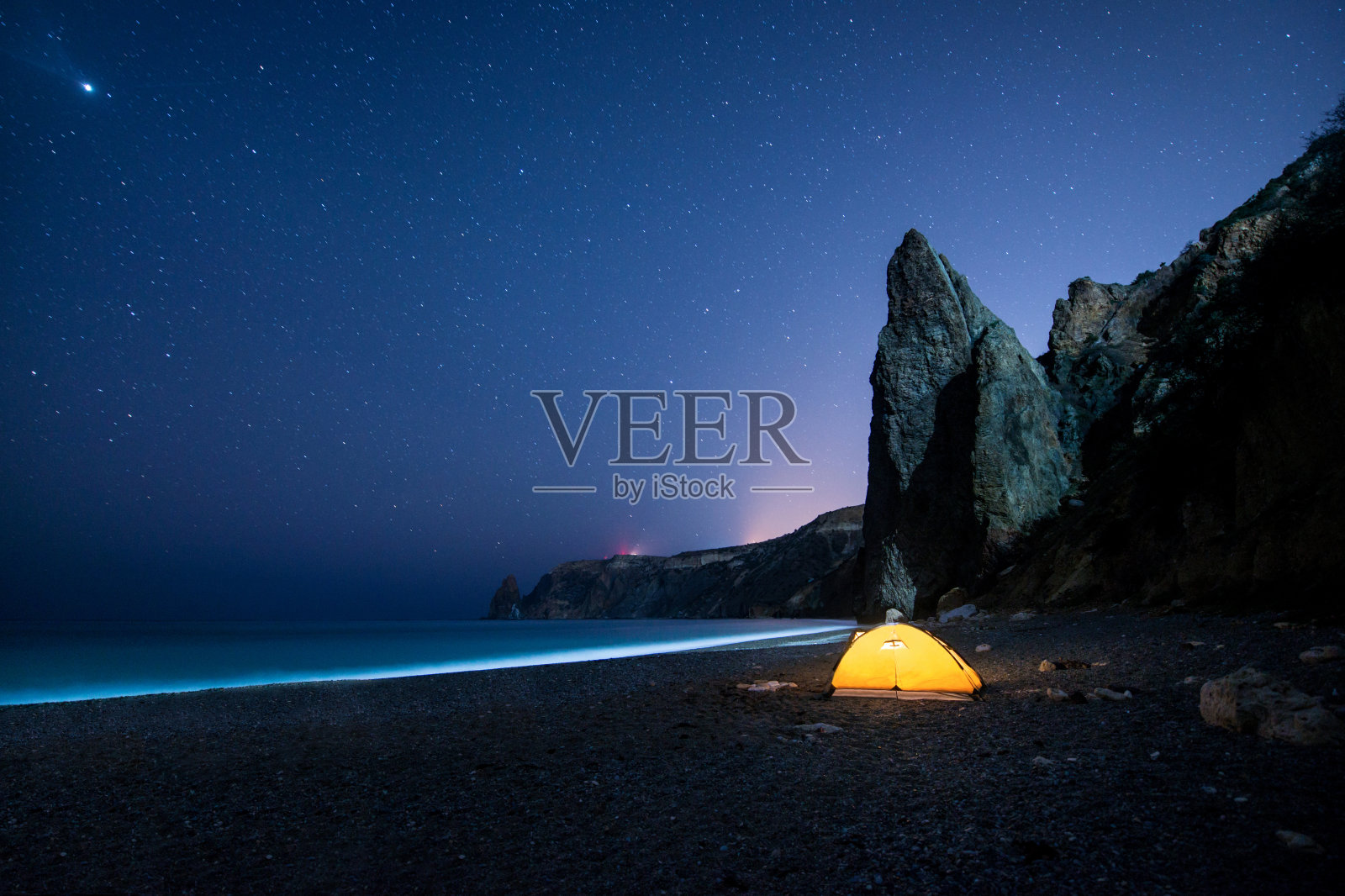 在繁星点点的夜空下，在美丽的海岸上有闪闪发光的帐篷和岩石照片摄影图片