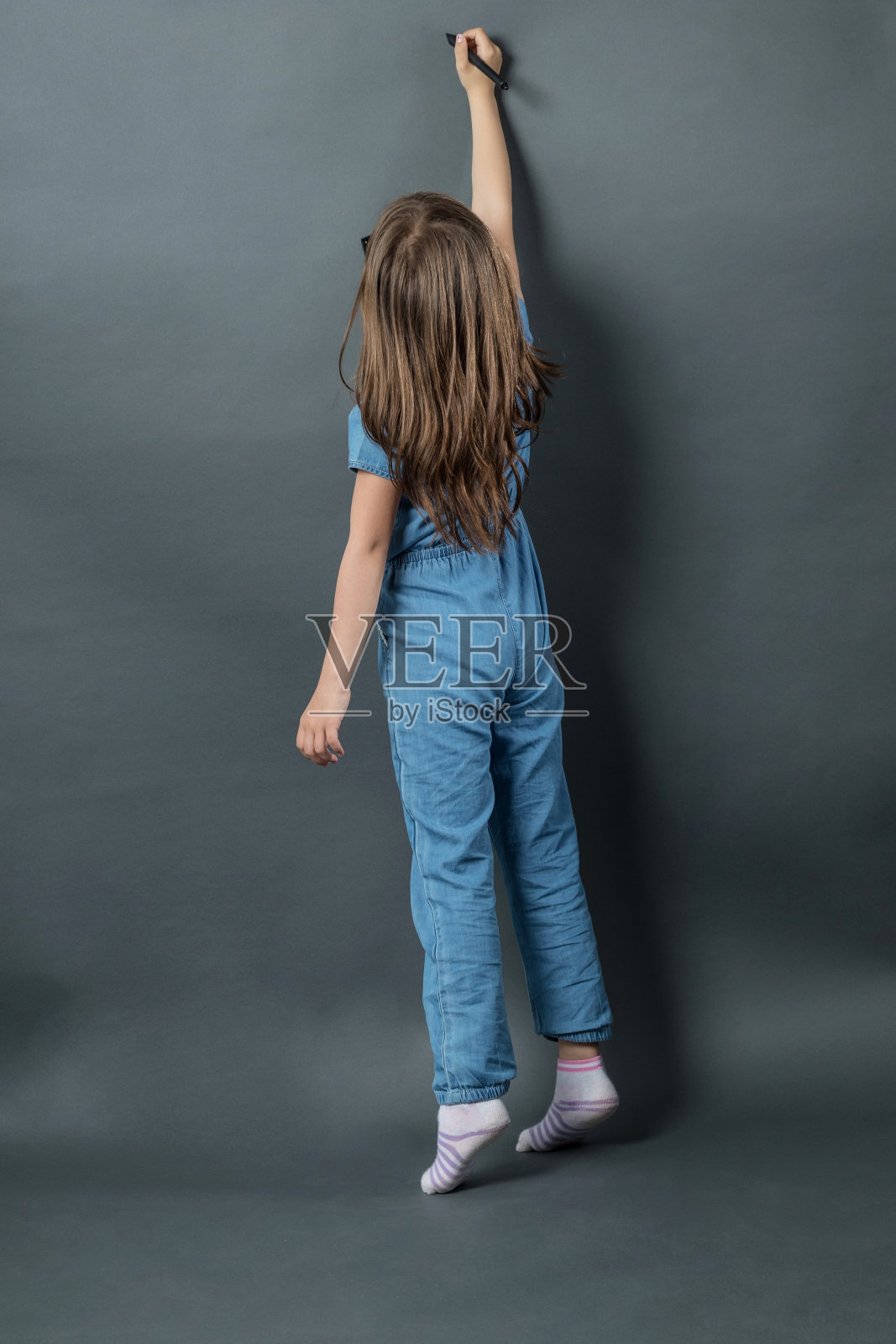 年轻的女孩踮着脚尖在灰色的背景下写作照片摄影图片