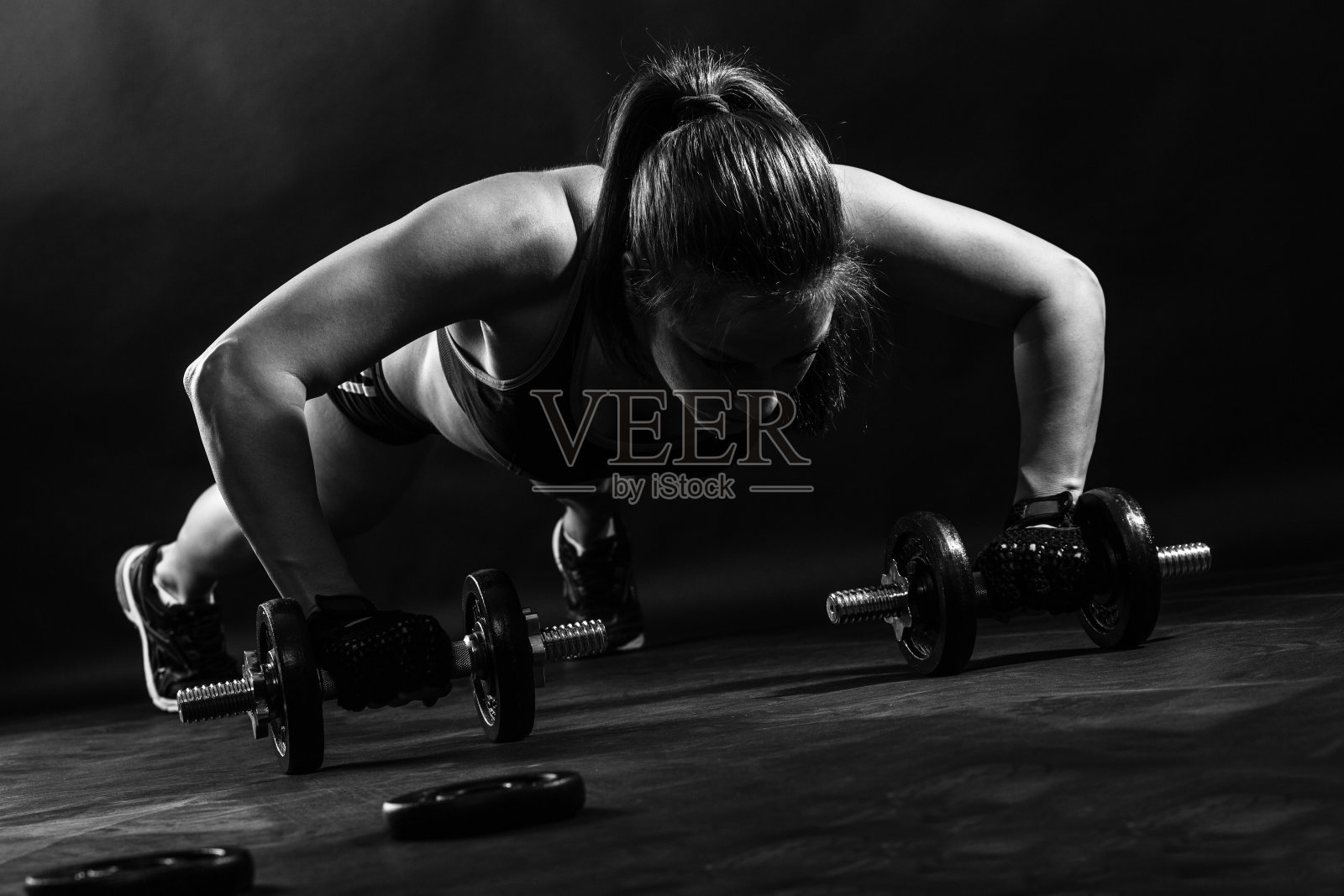 女性健美运动员举着哑铃孤立在黑色背景，黑色和白色。照片摄影图片