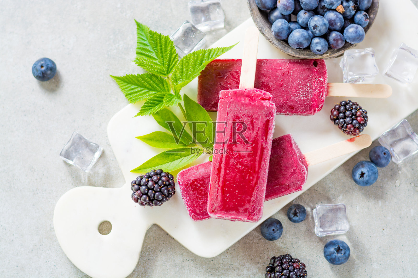 新鲜的夏季野生蓝莓和覆盆子，自制冰沙冰淇淋冰棒在大理石盘子照片摄影图片