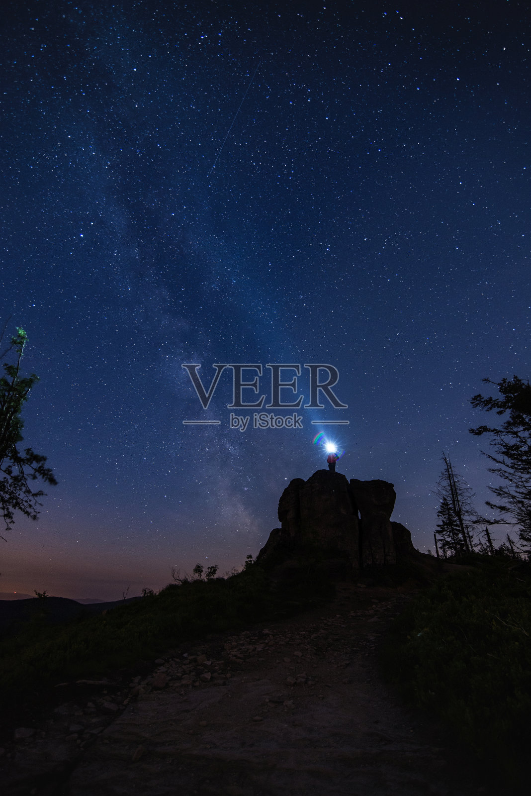 游客站在岩石上，用手电筒照亮夜空照片摄影图片