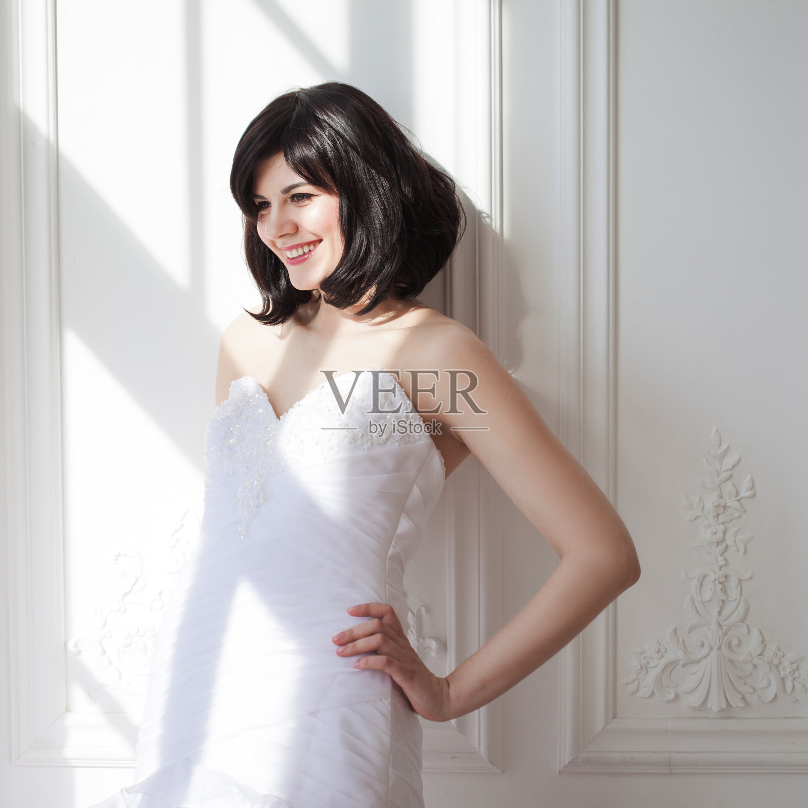 年轻迷人的画像与短头发在婚礼礼服。她站在白色的墙壁上，右边没有空间。快乐的新娘。照片摄影图片