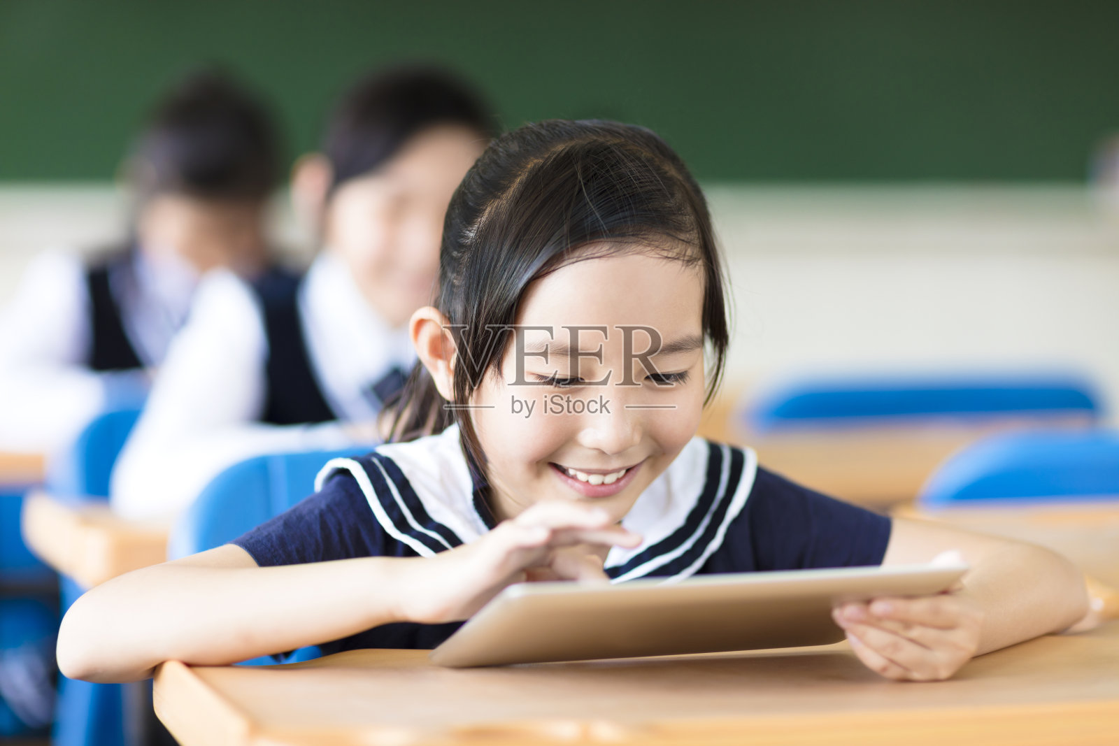 微笑的小女孩在教室里使用平板电脑照片摄影图片