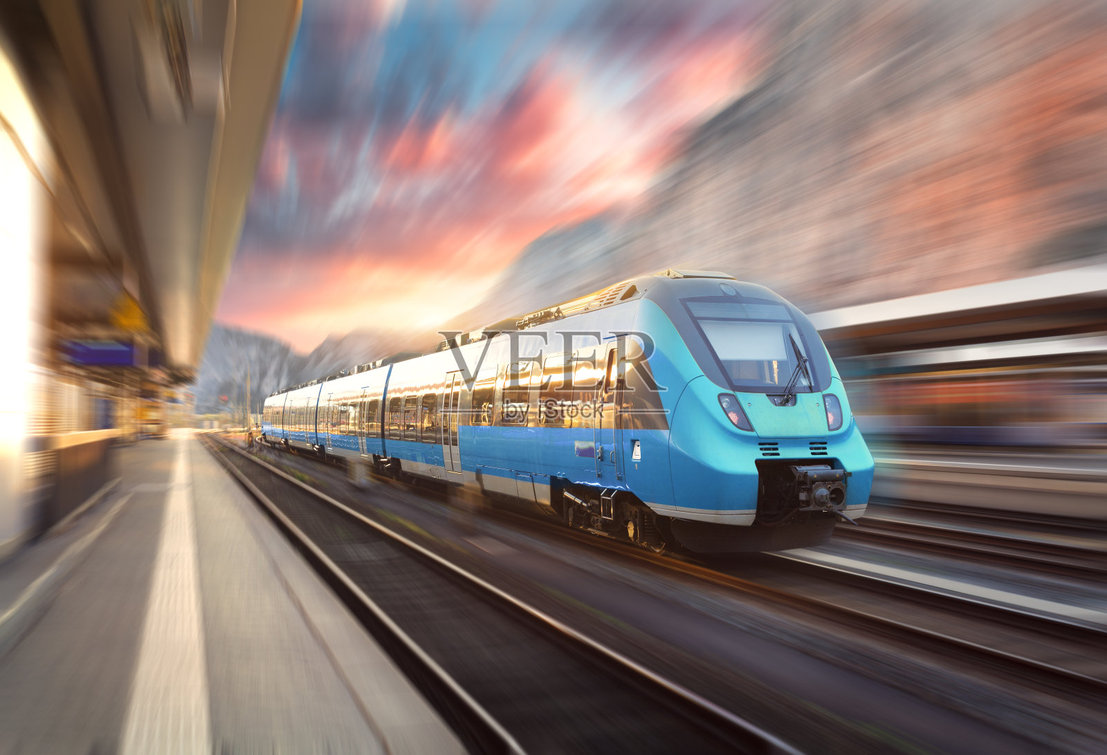 日落时分，一列惊人的火车在火车站上行驶。现代欧洲城际列车站台上的运动模糊效果。铁路上有蓝色客运列车的工业景观照片摄影图片