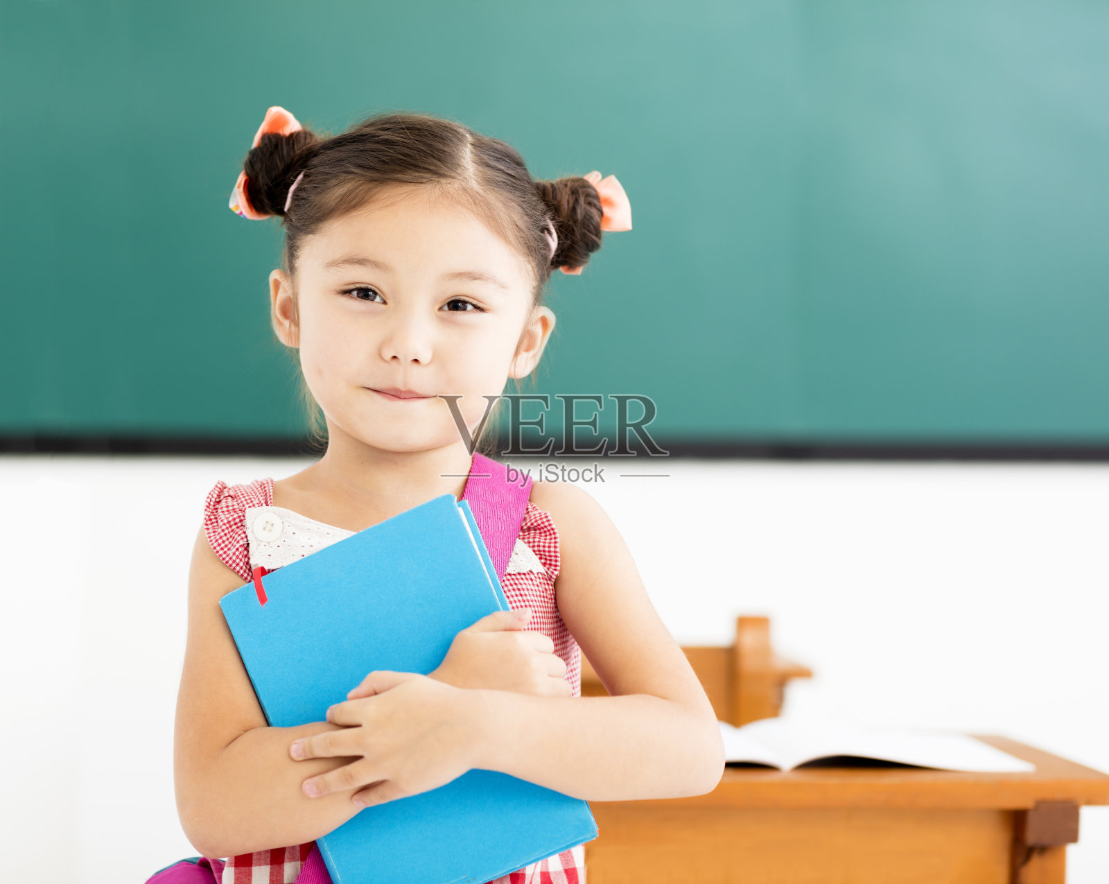 快乐的小女孩拿着书在教室里照片摄影图片