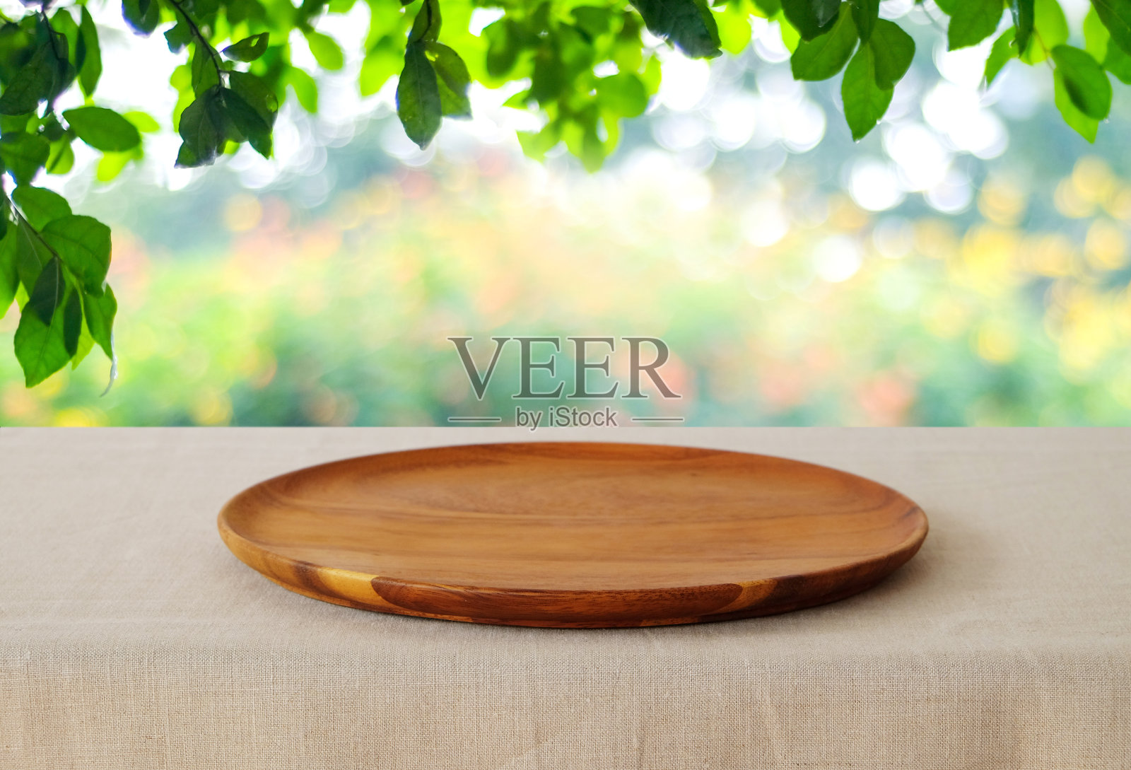 空的圆形木托盘在桌子上亚麻桌布上模糊的树背景，食物和产品显示蒙太奇，模板照片摄影图片