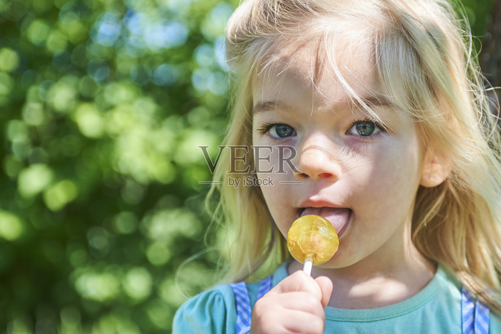 夏日里，金发碧眼的小女孩拿着棒棒糖在草地上休息照片摄影图片