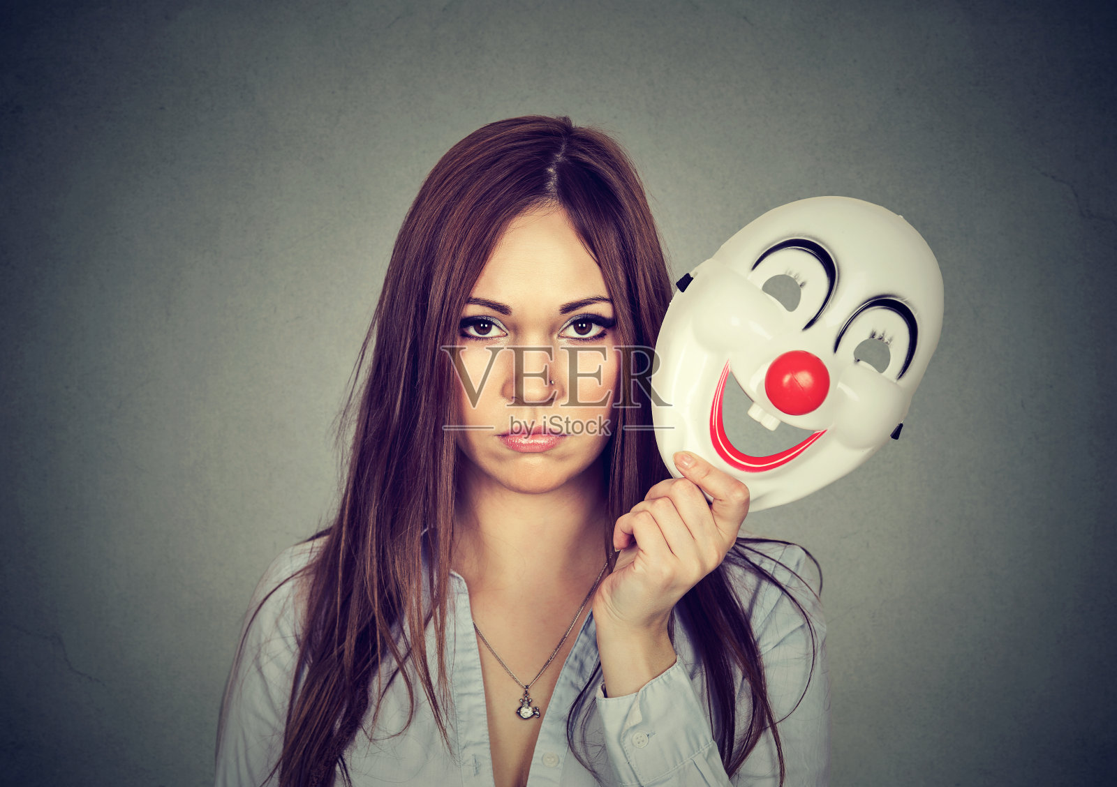 年轻苦恼的女人带着悲伤的表情摘下小丑面具照片摄影图片