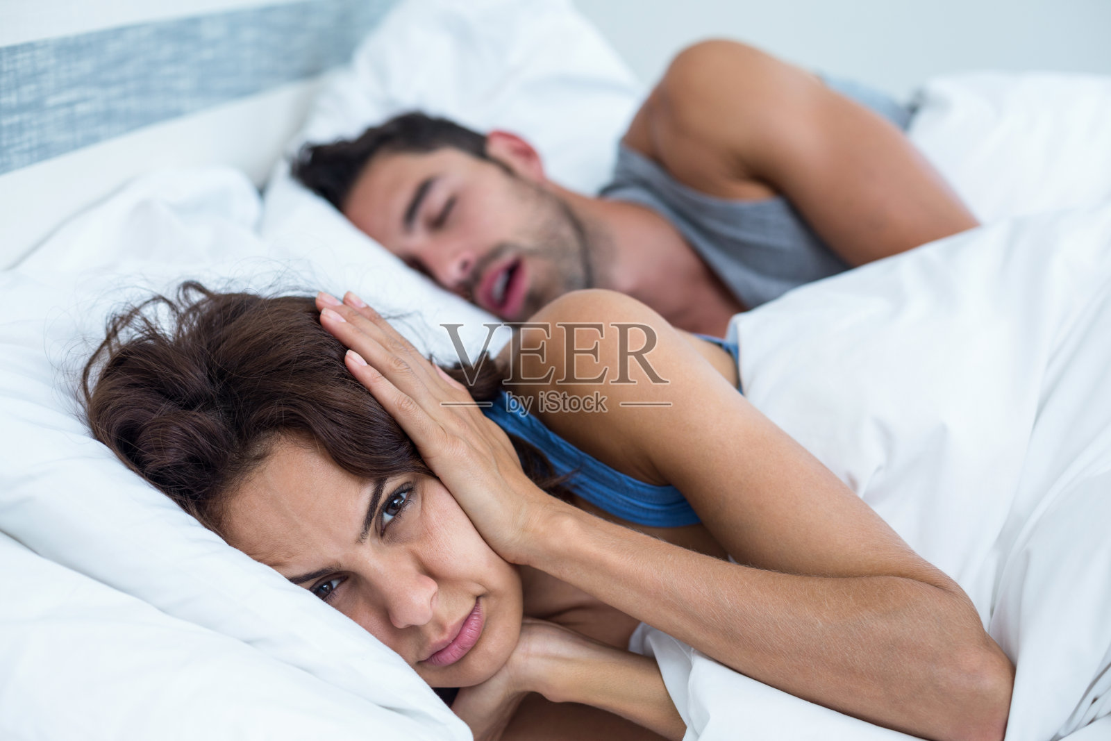 女人用手挡住耳朵，男人在床上打鼾照片摄影图片
