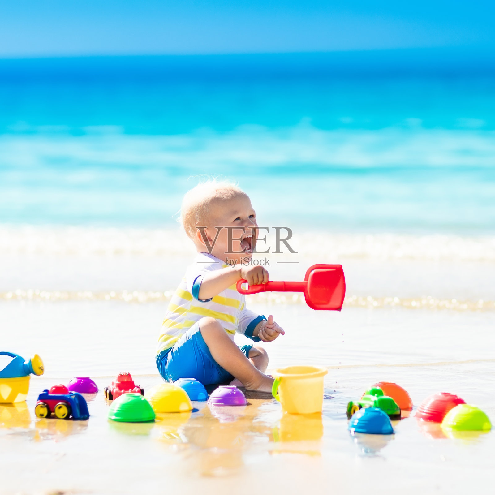 宝宝在热带海滩上玩，在沙子里挖洞照片摄影图片
