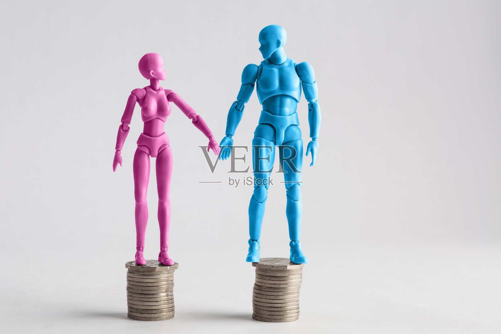 男性和女性雕像手牵着手看着对方，站在相等的硬币堆上。收入平等的概念与复制空间照片摄影图片
