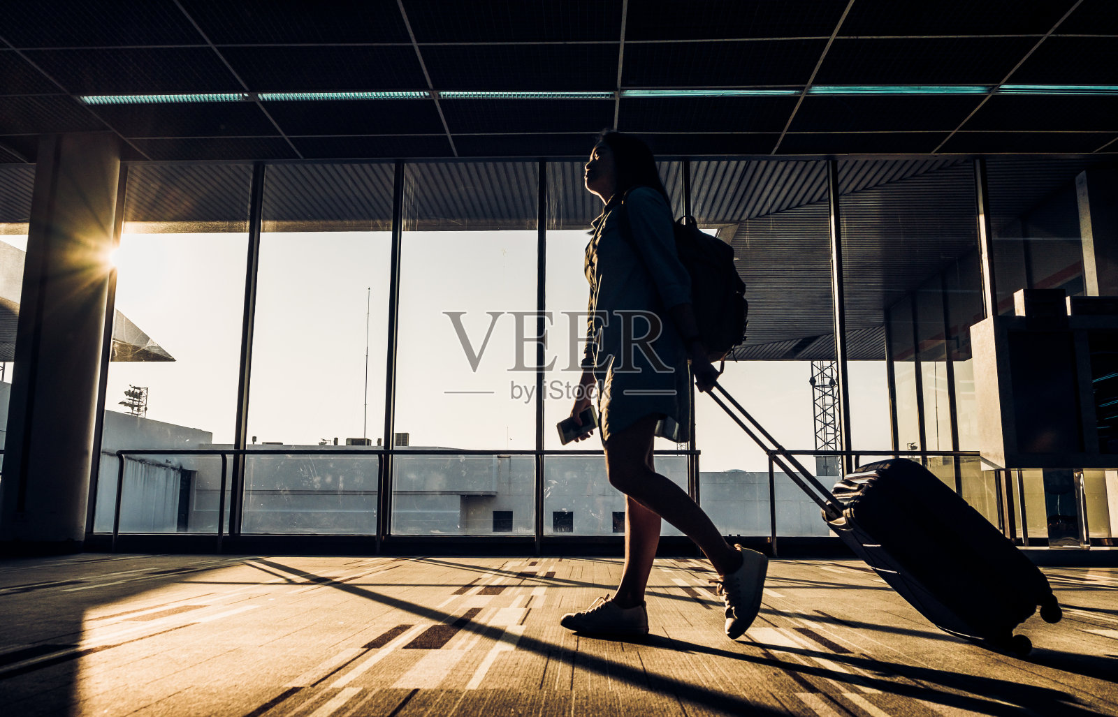 日出时分，年轻女孩带着行李走在机场航站楼窗口的剪影，旅行理念，旅行生活方式照片摄影图片
