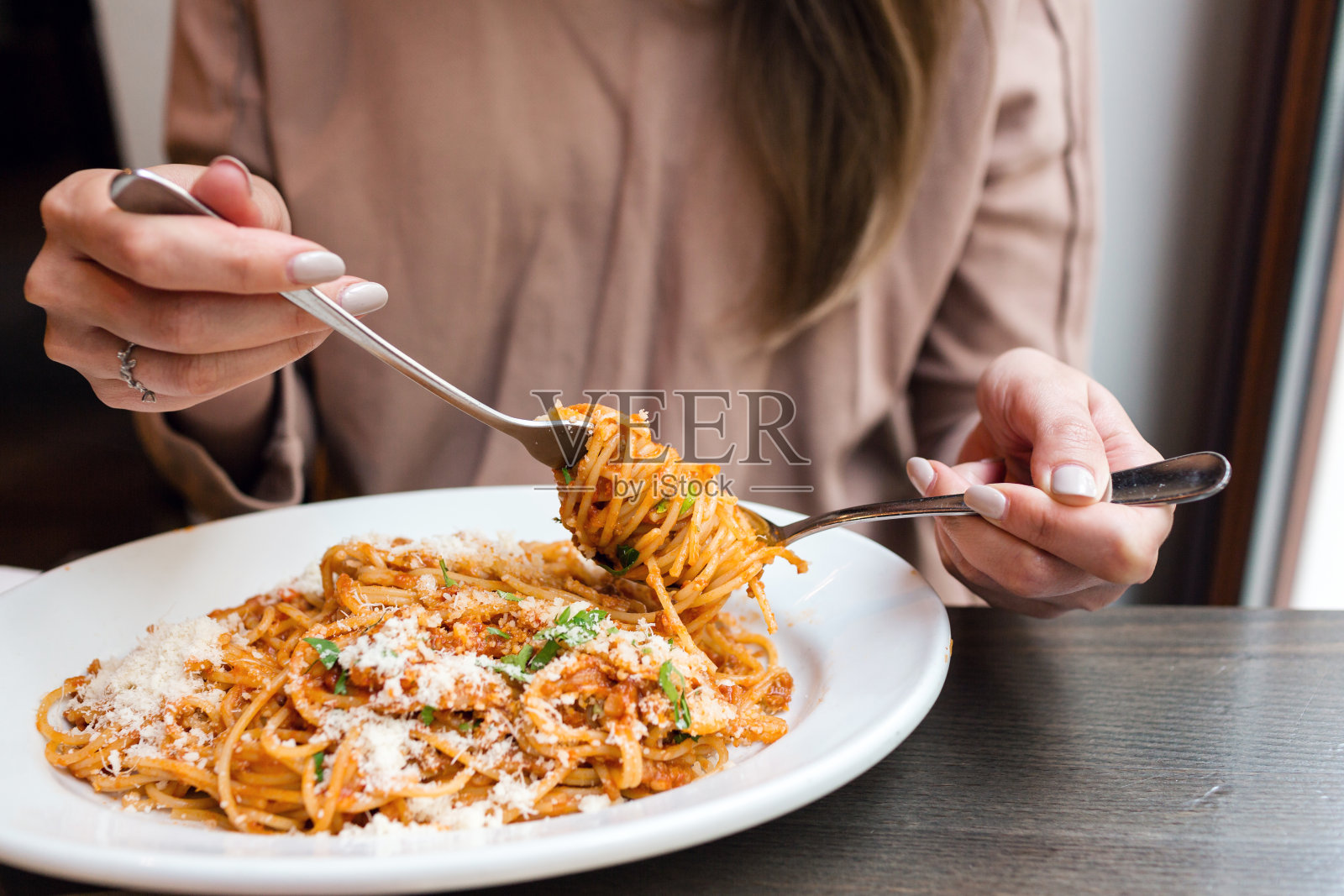 女孩吃意大利面加西红柿和肉。特写肉酱面，用勺子把它绕在叉子上。帕玛森芝士照片摄影图片