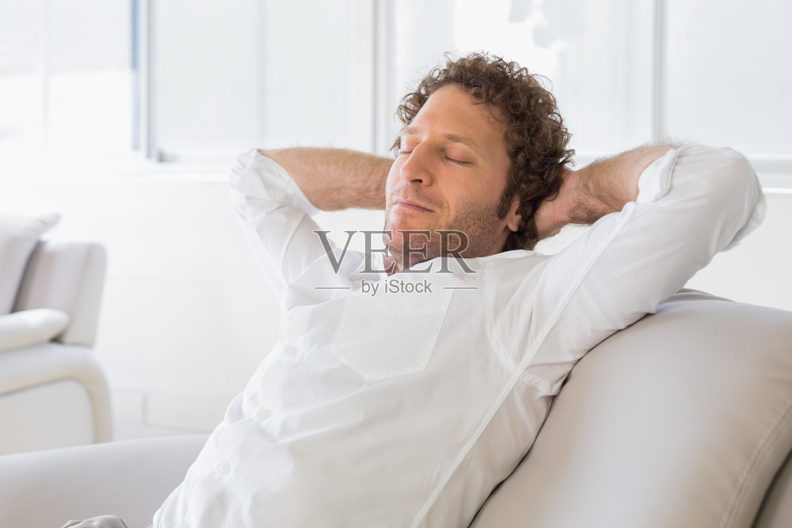 放松的男人坐在家里，双手放在脑后照片摄影图片