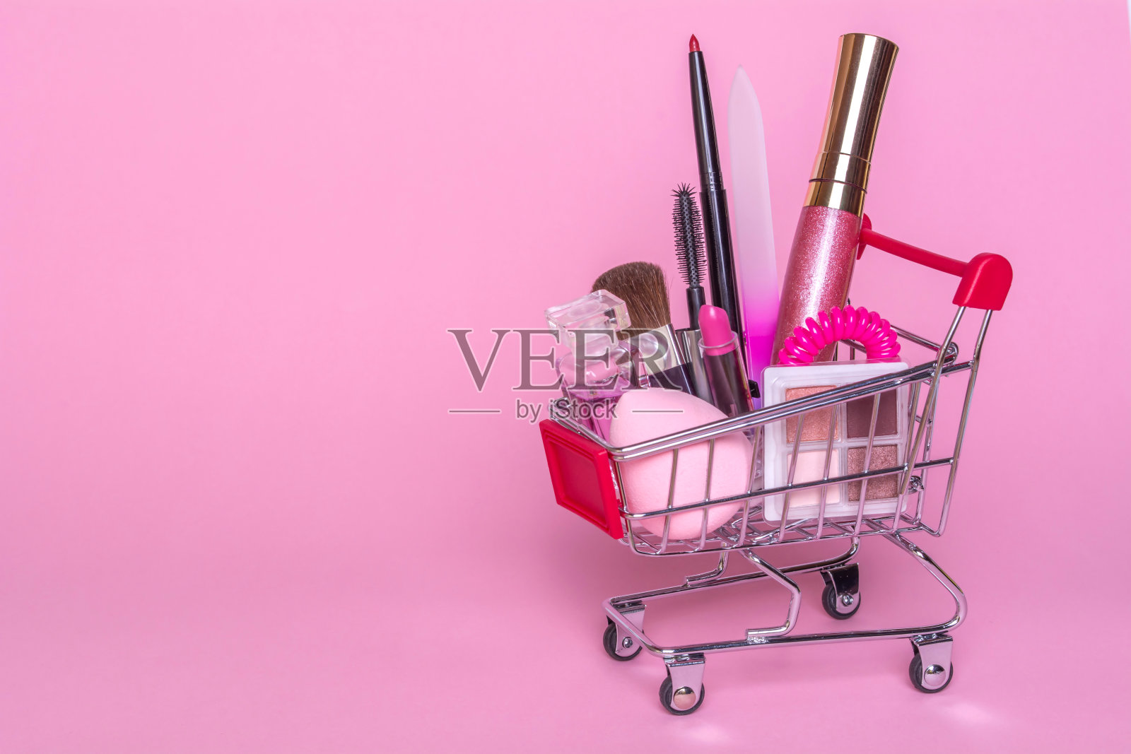 粉色背景的化妆品购物车。香水,刷,睫毛膏照片摄影图片