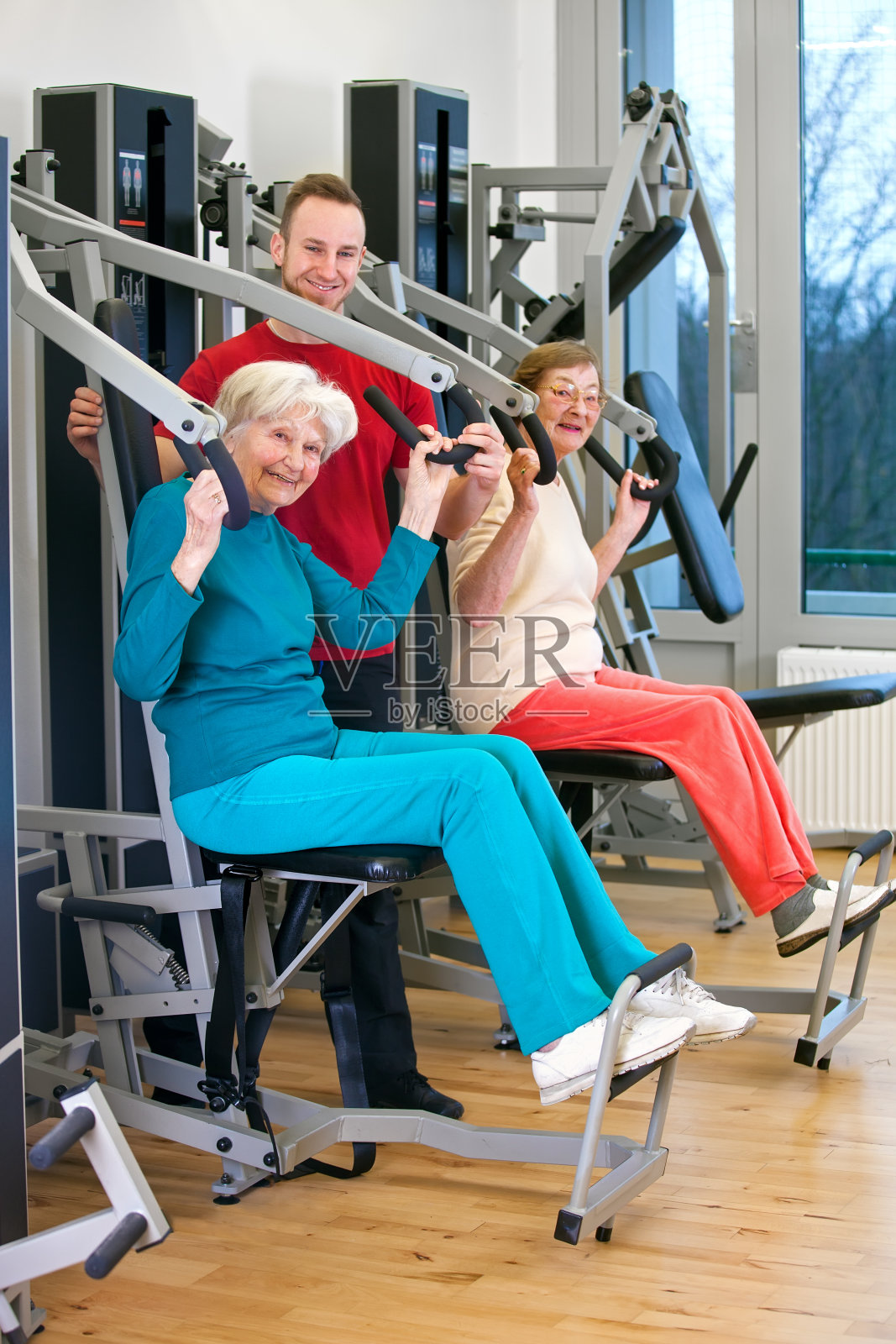 在教练的帮助下，在健身房快乐的老妇人。照片摄影图片