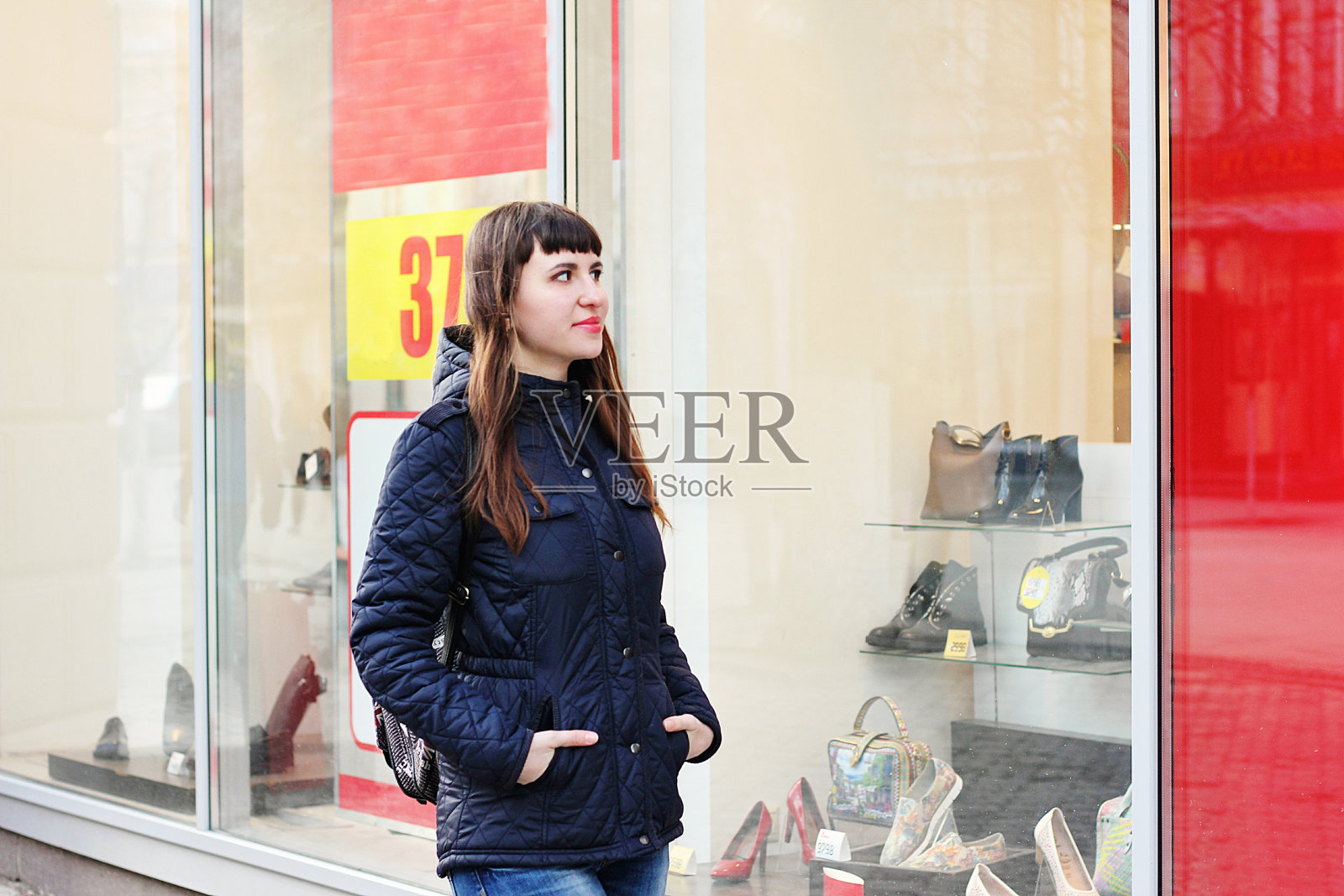 一位漂亮的女孩正站在一家时装店的橱窗旁。照片摄影图片