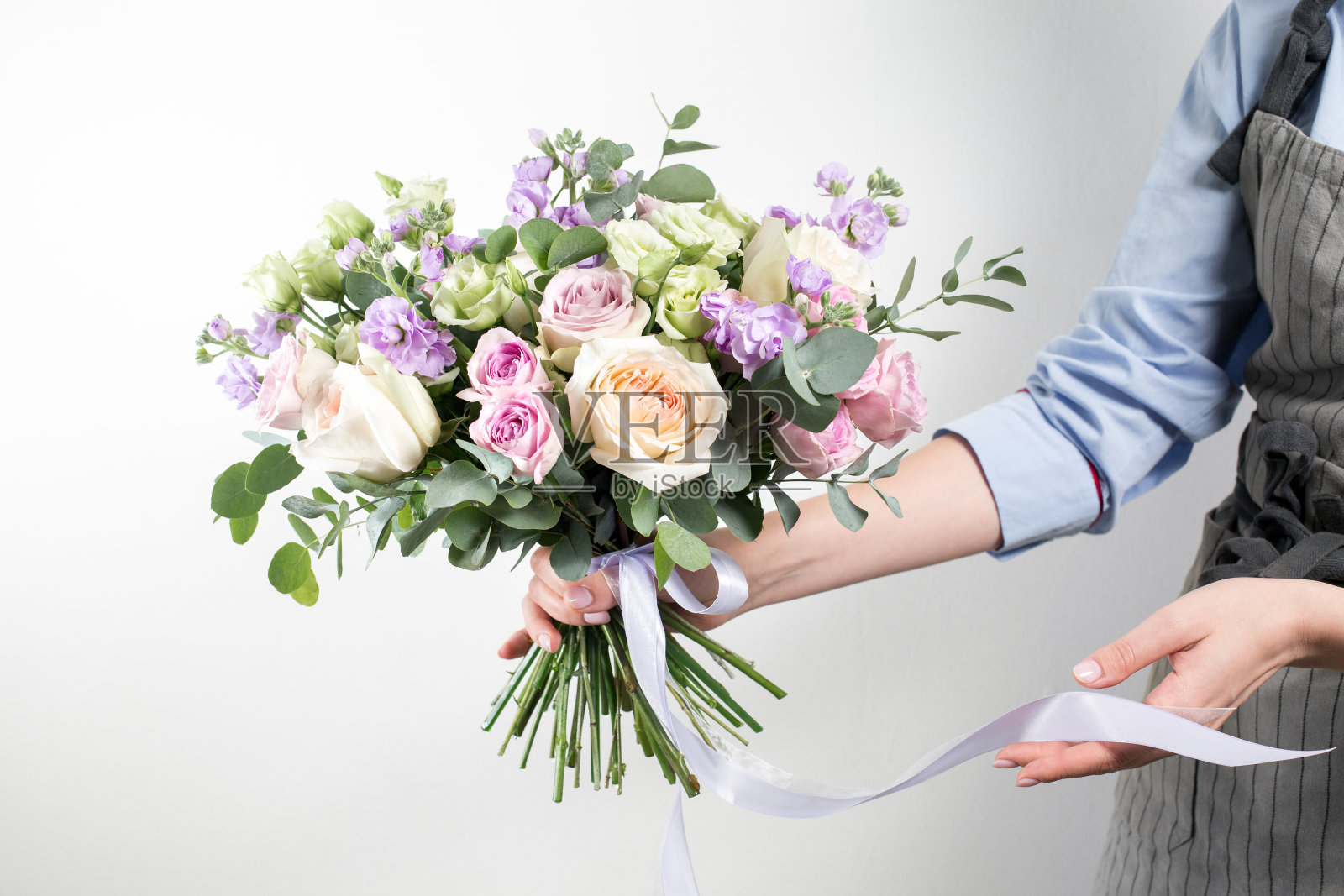 美丽的花束，由不同的鲜花在年轻女孩的手中。色彩缤纷的混花。蓝色衬衫和灰色围裙的工作服照片摄影图片