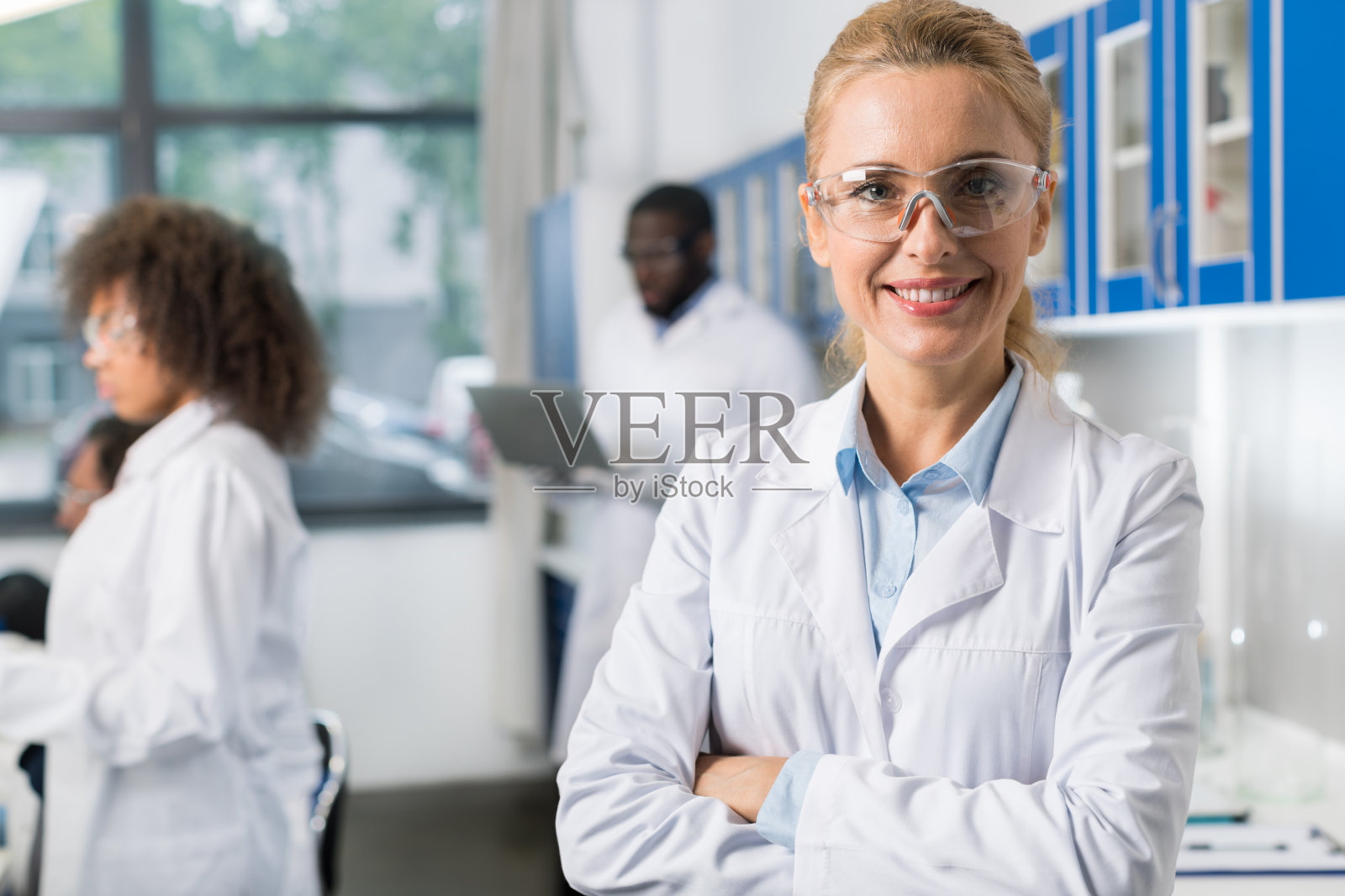 微笑的女人在现代实验室穿着白色外套和保护眼镜的肖像，女科学家在忙碌的研究团队照片摄影图片
