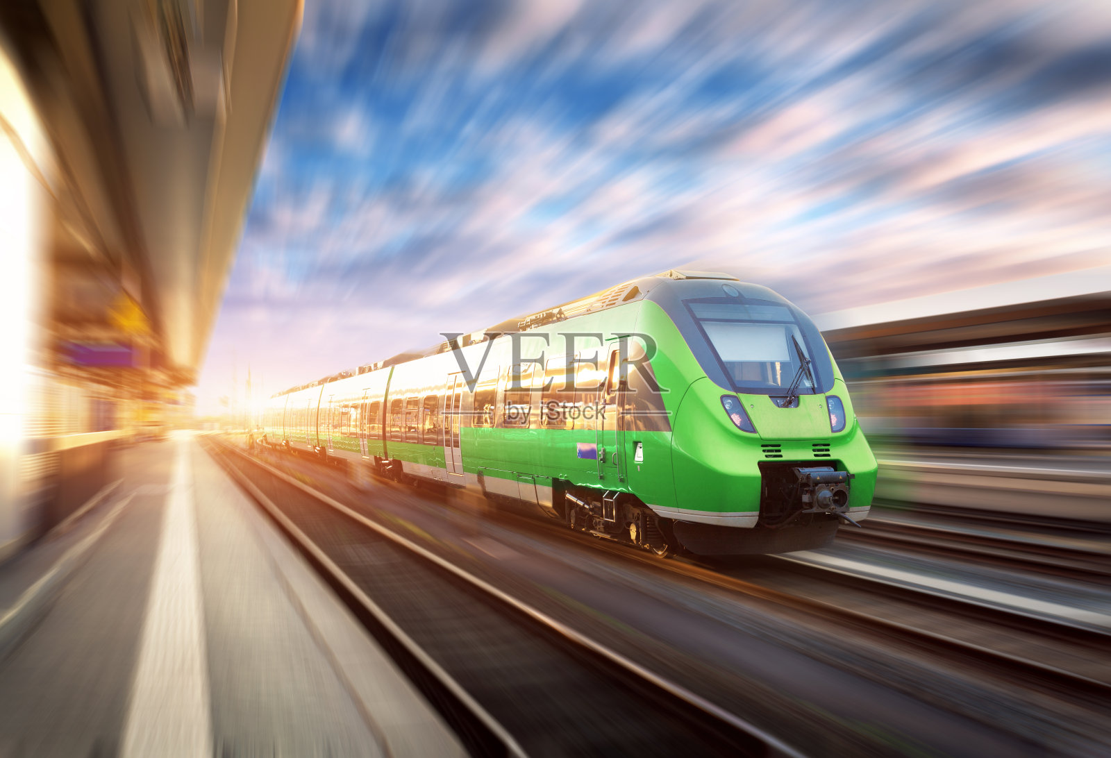 日落时分，欧洲火车站上运行的高速列车。美丽的绿色现代火车在铁路站台与运动模糊效果。铁路上有客运列车的工业场景照片摄影图片