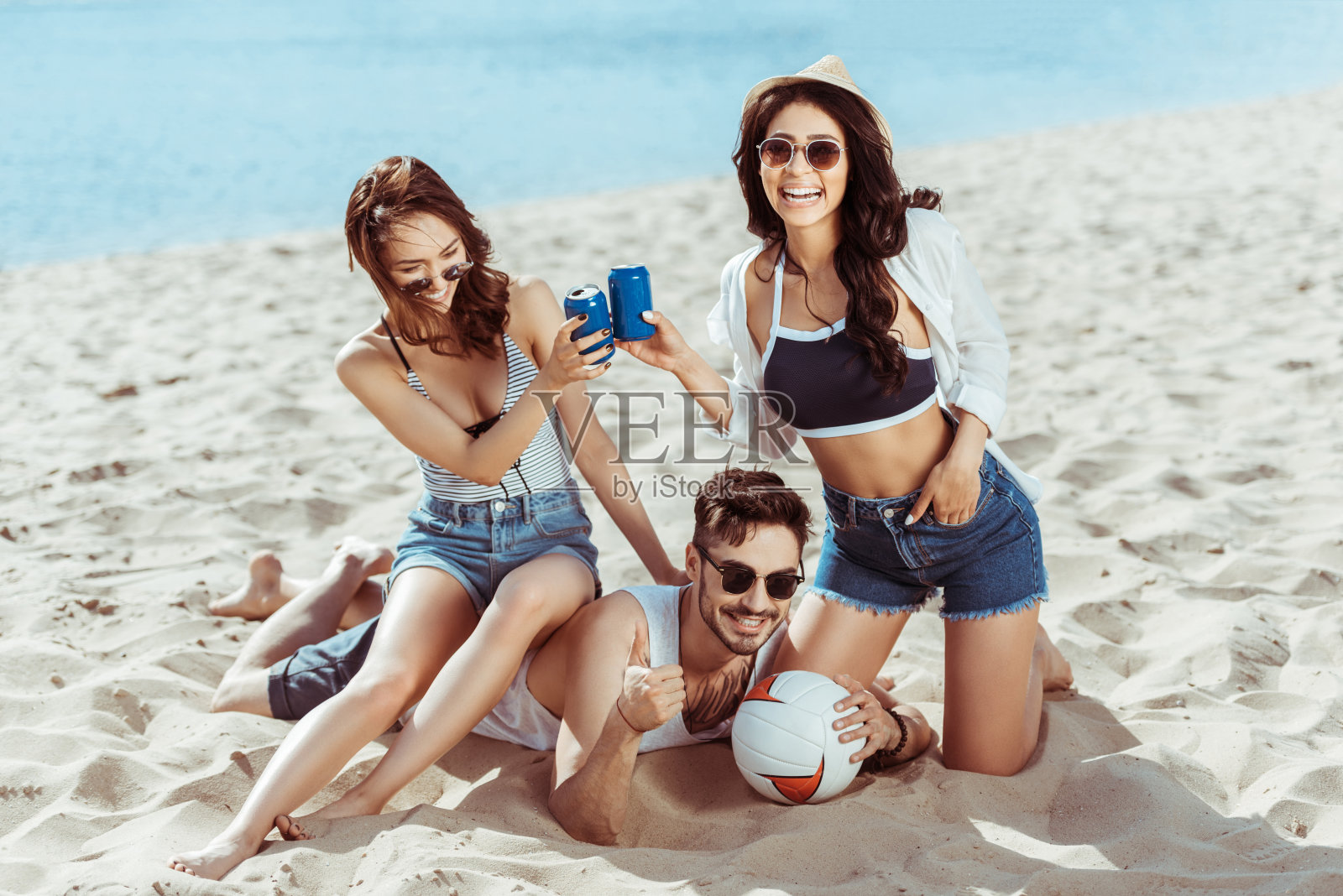 欢乐的多文化的朋友们带着排球和汽水罐在沙滩上休息照片摄影图片