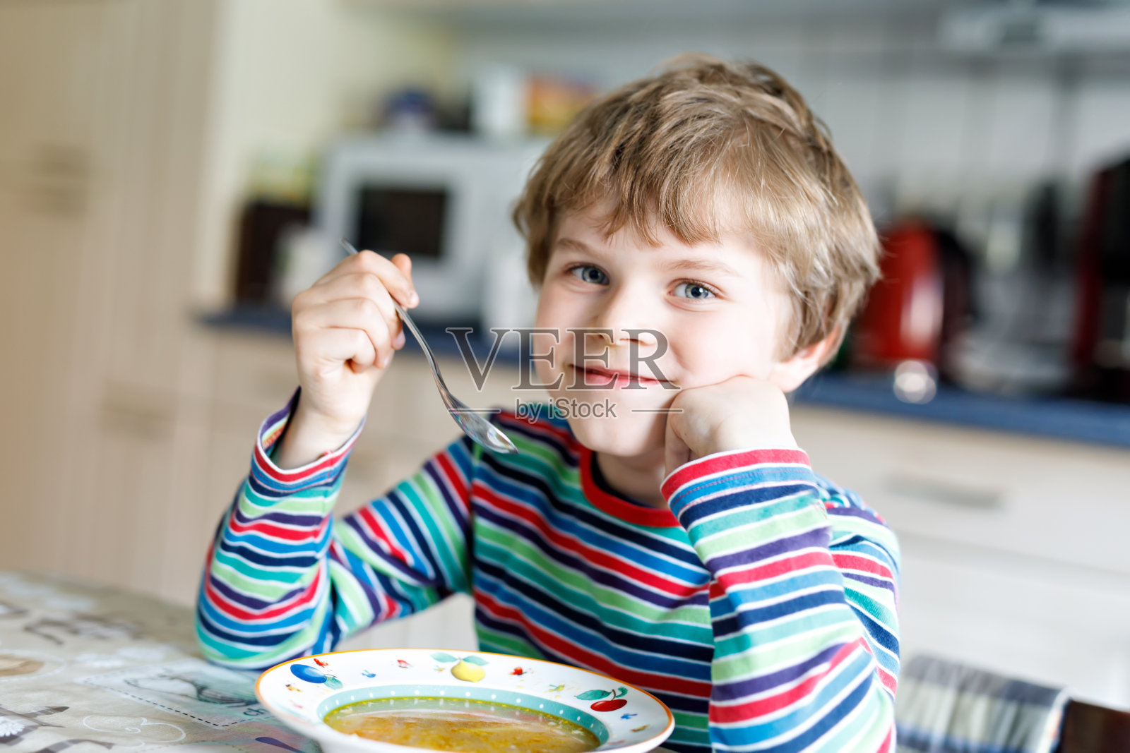 可爱的小男孩在室内吃蔬菜汤。照片摄影图片