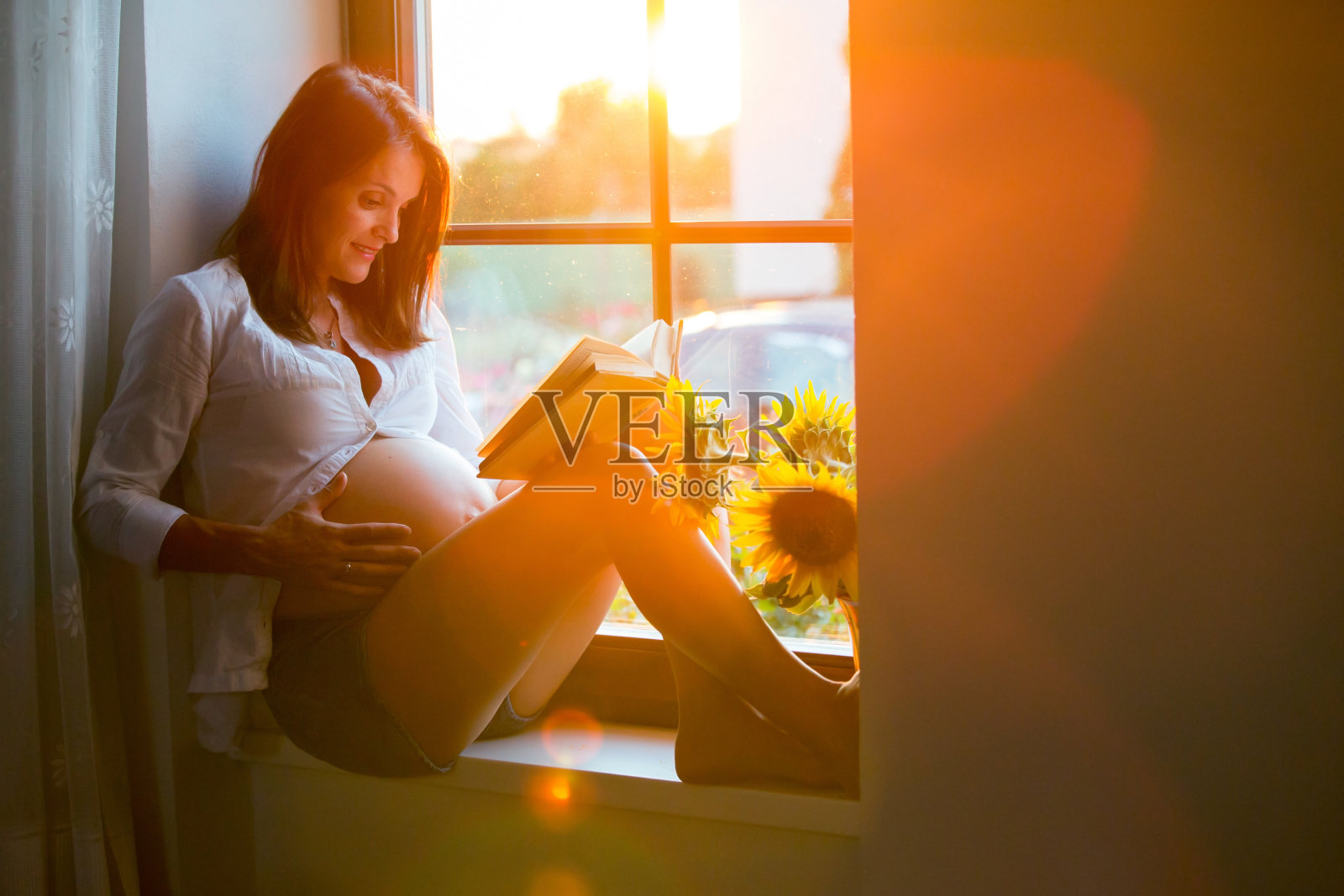 美丽的孕妇，坐在窗罩上，看书照片摄影图片